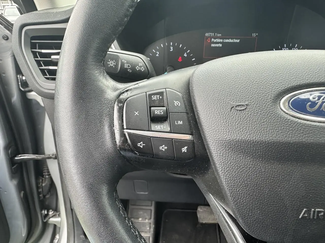 Gros plan sur le volant noir du Ford Kuga gris solaire 2020, avec commandes de régulateur de vitesse et tableau de bord partiel visible.