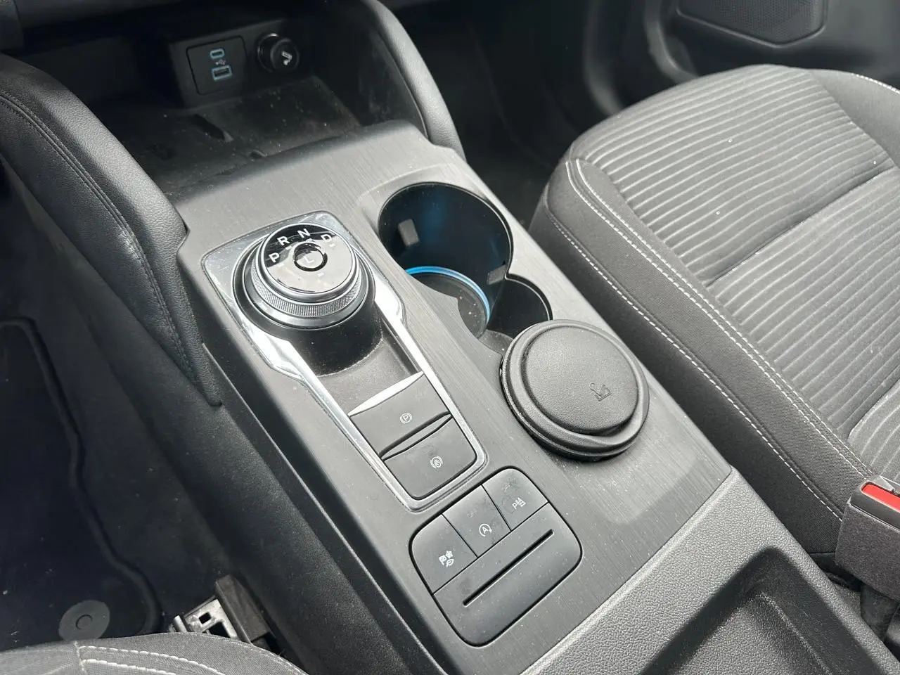 Gros plan sur la console centrale noire du Ford Kuga 2020 avec sélecteur rotatif de vitesse et porte-gobelets.