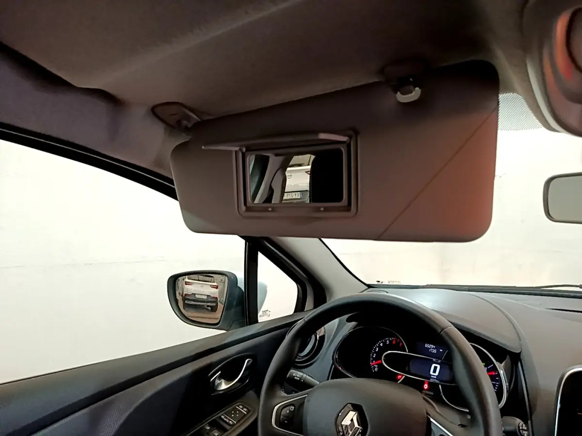 Vue intérieure côté conducteur de la Renault Clio Business blanche, volant cuir et pare-soleil avec miroir ouvert.