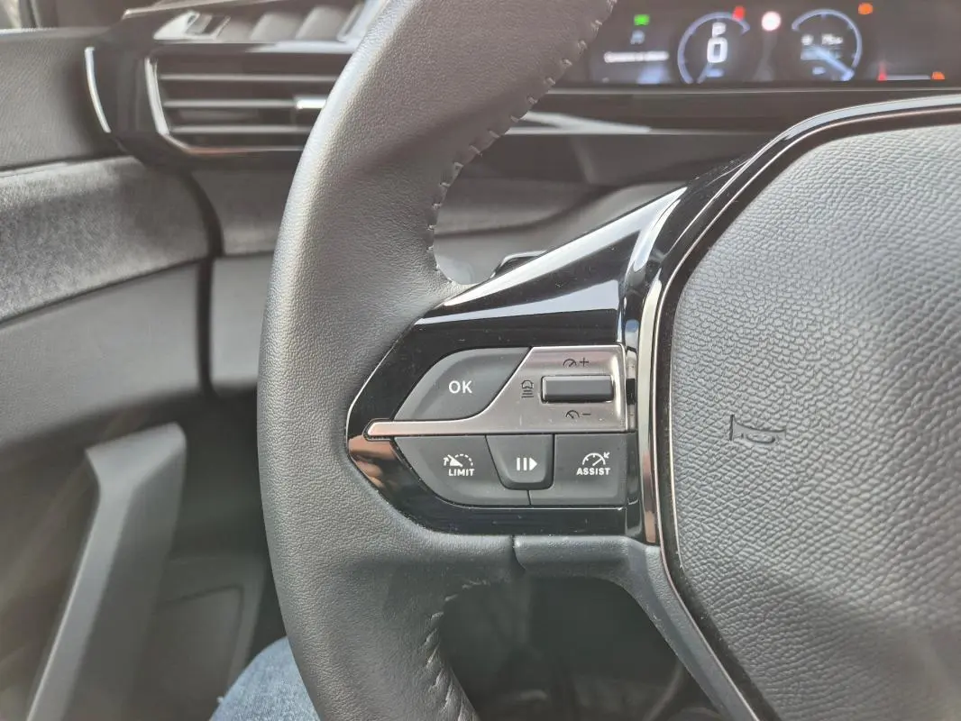 Gros plan sur le volant noir de la Peugeot 308 2024 avec commandes intégrées et tableau de bord numérique en arrière-plan.