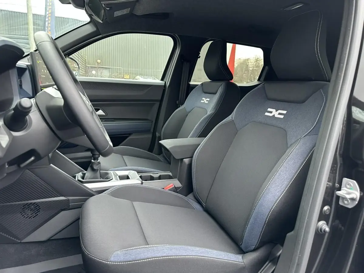 Vue intérieure côté conducteur du Dacia Duster noir 2025, sièges avant bi-matière avec logo DC brodé.