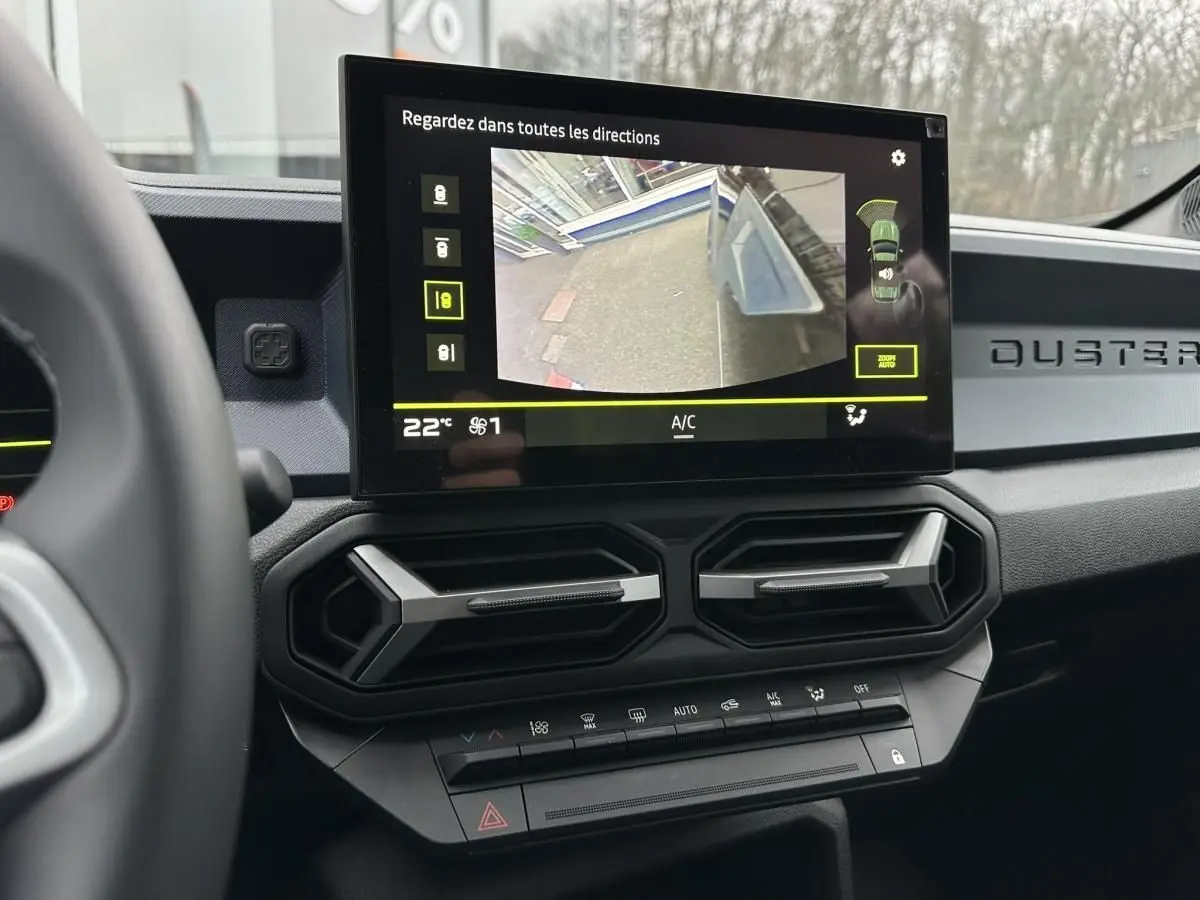 Vue intérieure du tableau de bord du Dacia Duster noir 2025, écran tactile affichant la caméra de recul et aérateurs hexagonaux.