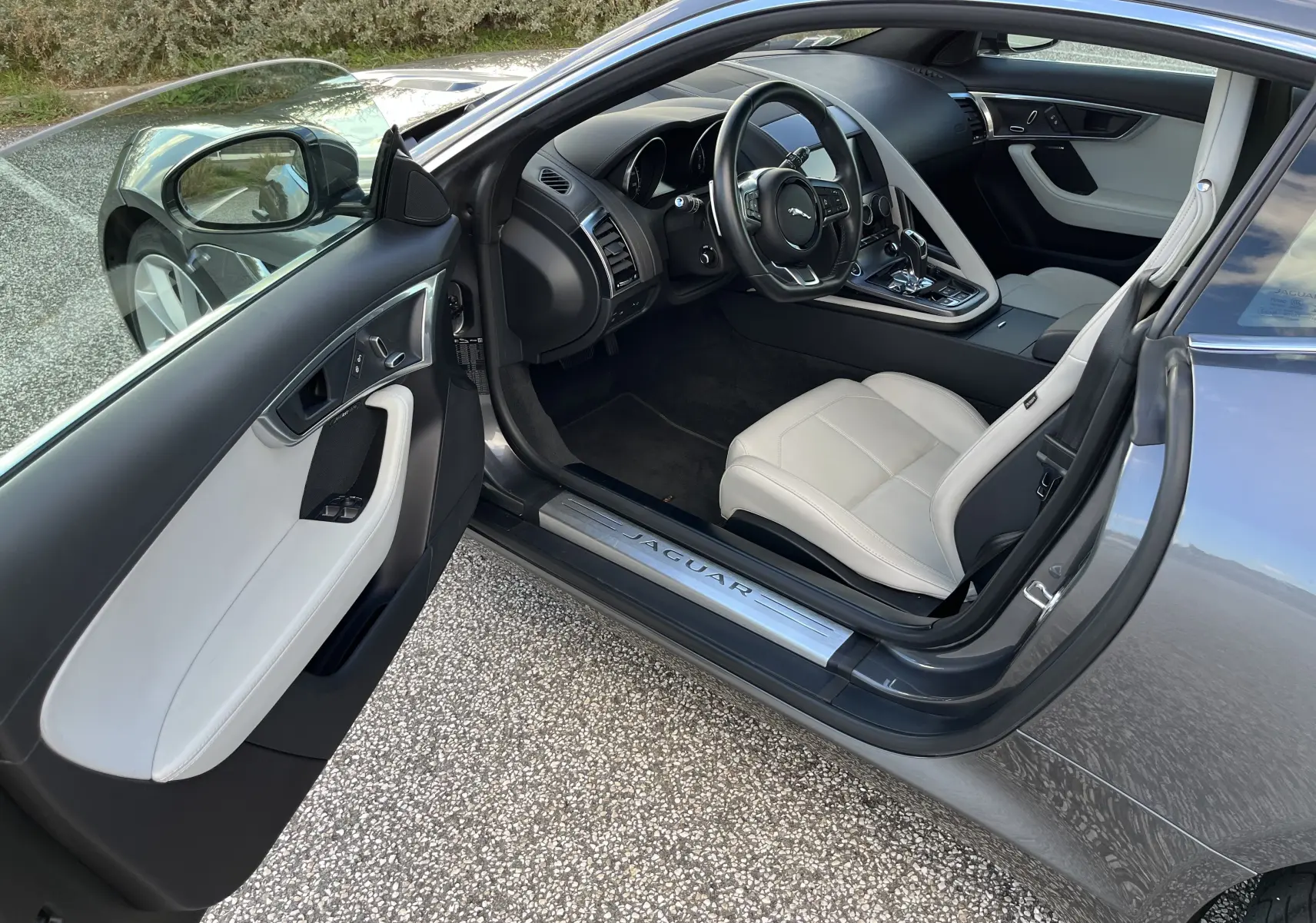 Vue côté gauche intérieur d'une Jaguar F-TYPE II Coupe 2.0T 2018 gris Corris, sièges sport cuir clair et tableau de bord moderne.