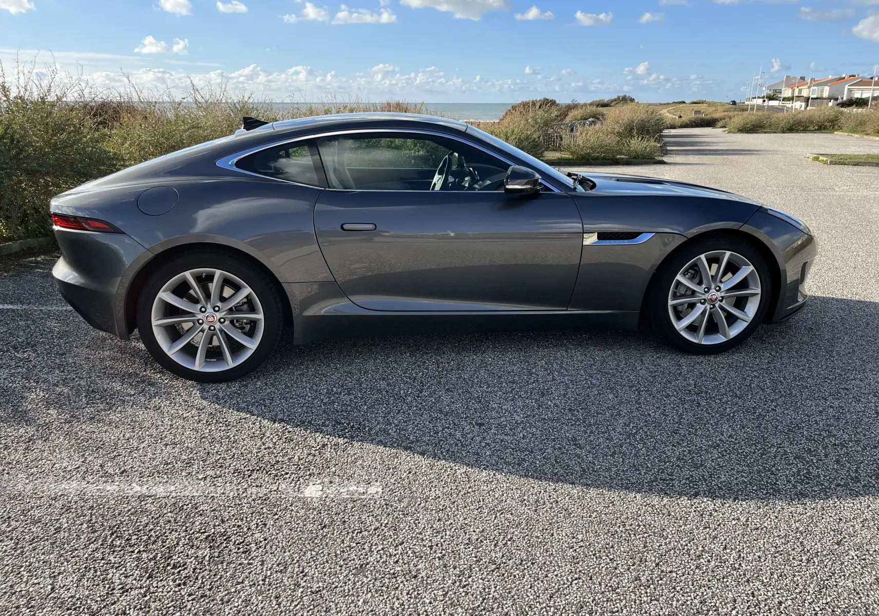 Vue de profil côté gauche d'une Jaguar F-TYPE II Coupé 2.0T 300 BVA8 gris Corris, avec jantes 19 pouces et lignes sportives élégantes.