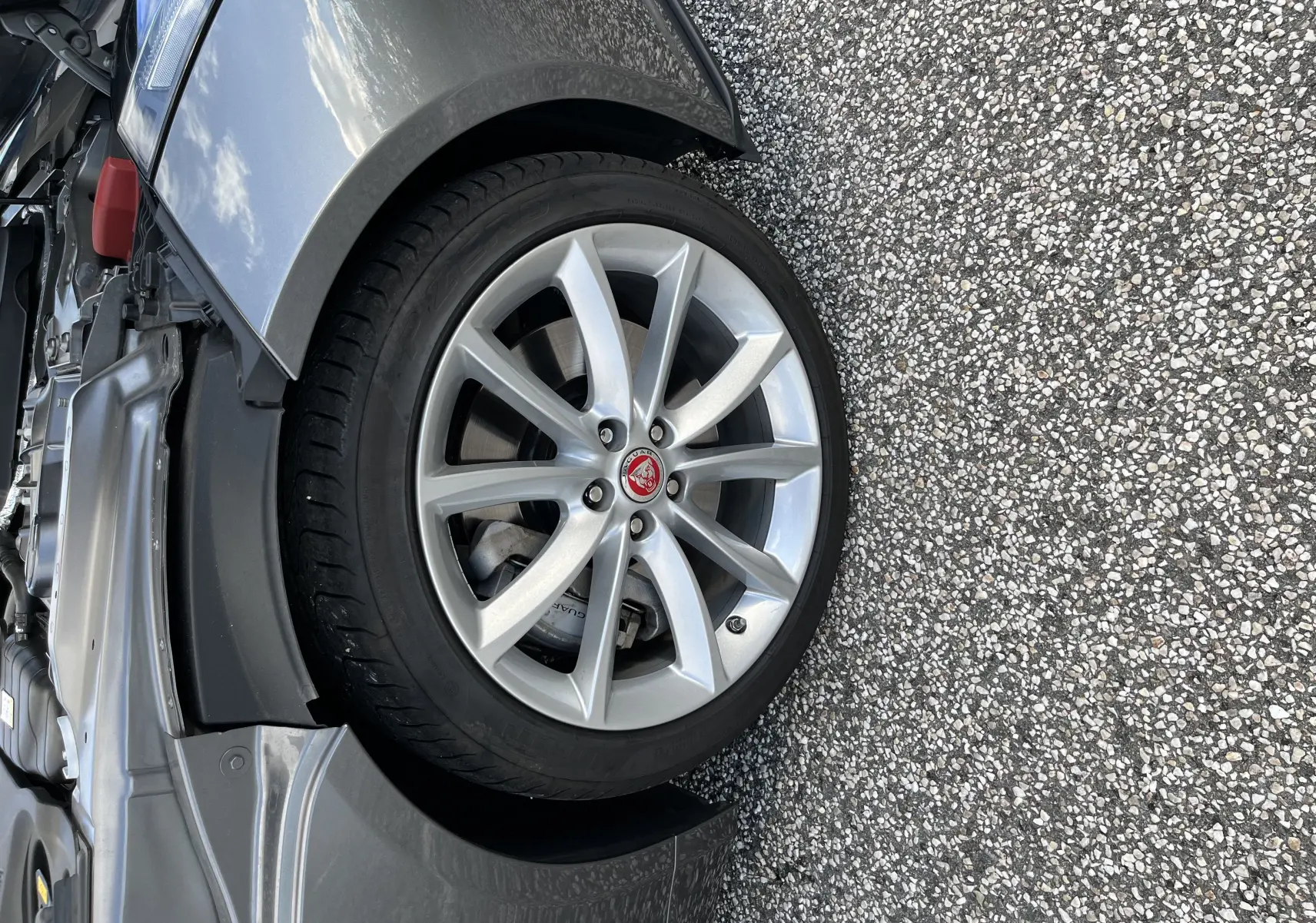Gros plan sur la roue avant gauche de la Jaguar F-TYPE gris Corris, jante 19 pouces 10 branches avec logo Jaguar rouge.