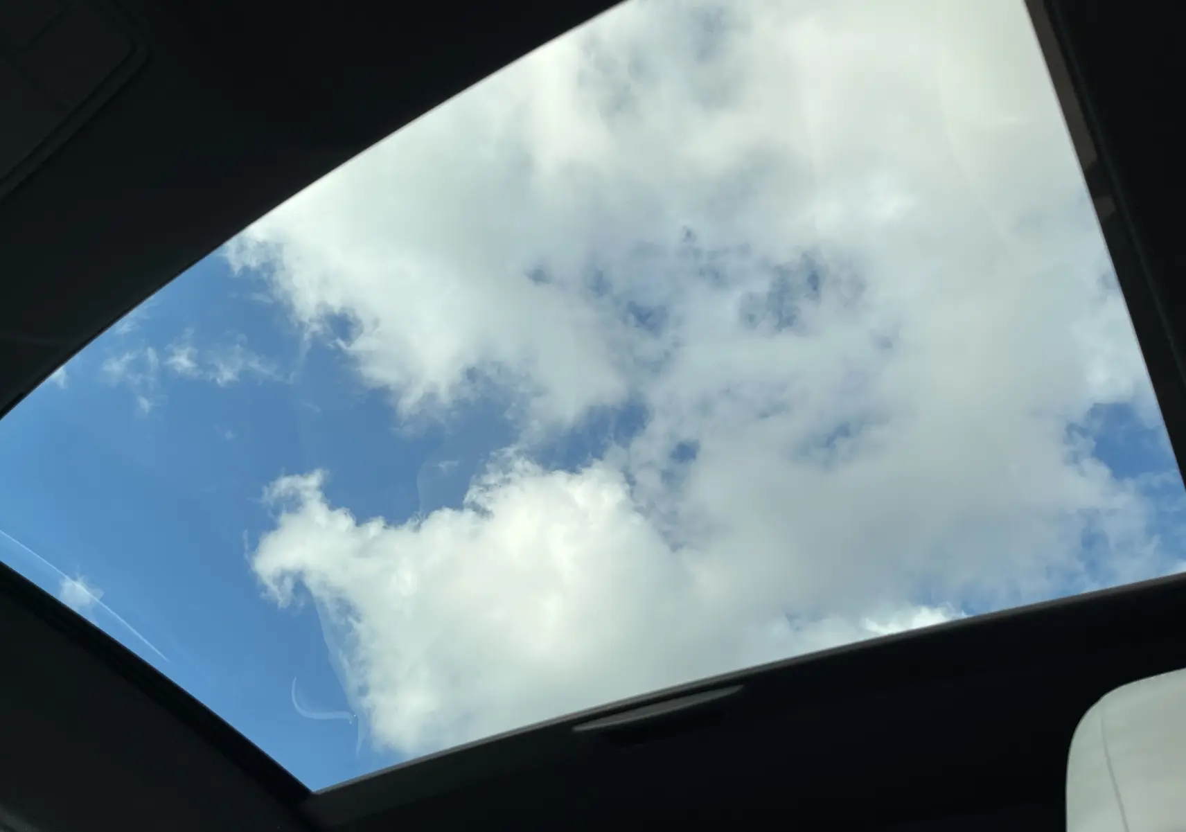 Vue intérieure du toit ouvrant panoramique de la Jaguar F-TYPE II Coupé 2.0T 300 BVA8, ciel bleu avec nuages visibles.