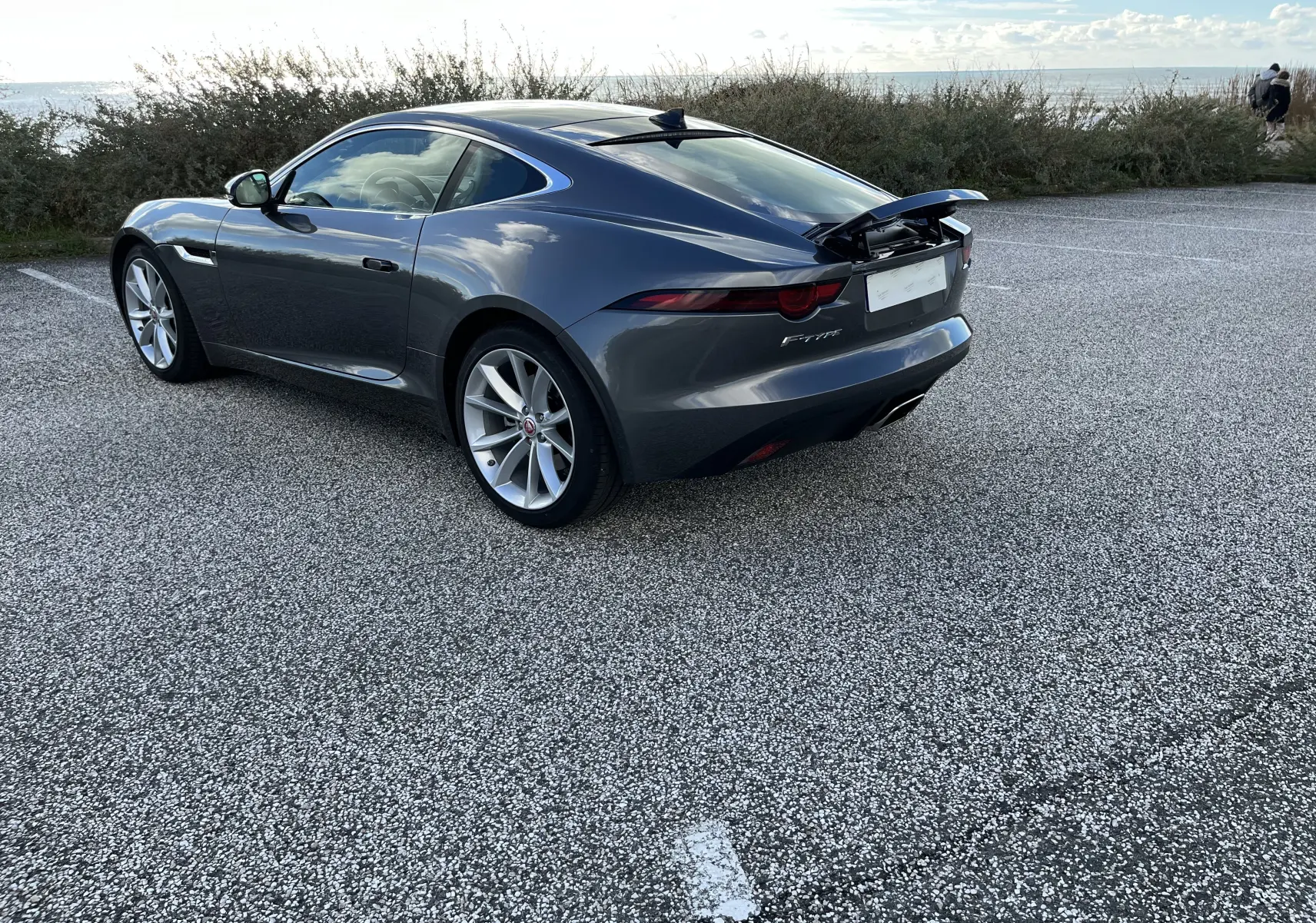 Jaguar F-TYPE II Coupé gris Corris vue 3/4 arrière droit avec aileron arrière relevé et jantes 19 pouces.