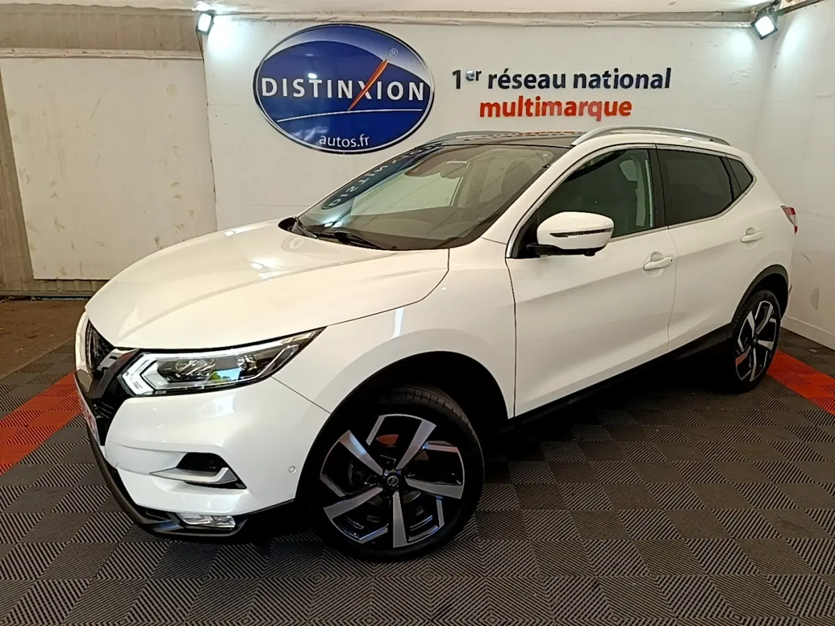 Nissan Qashqai blanc en 3/4 avant droit, avec jantes alliage noires et toit vitré visible en intérieur showroom.