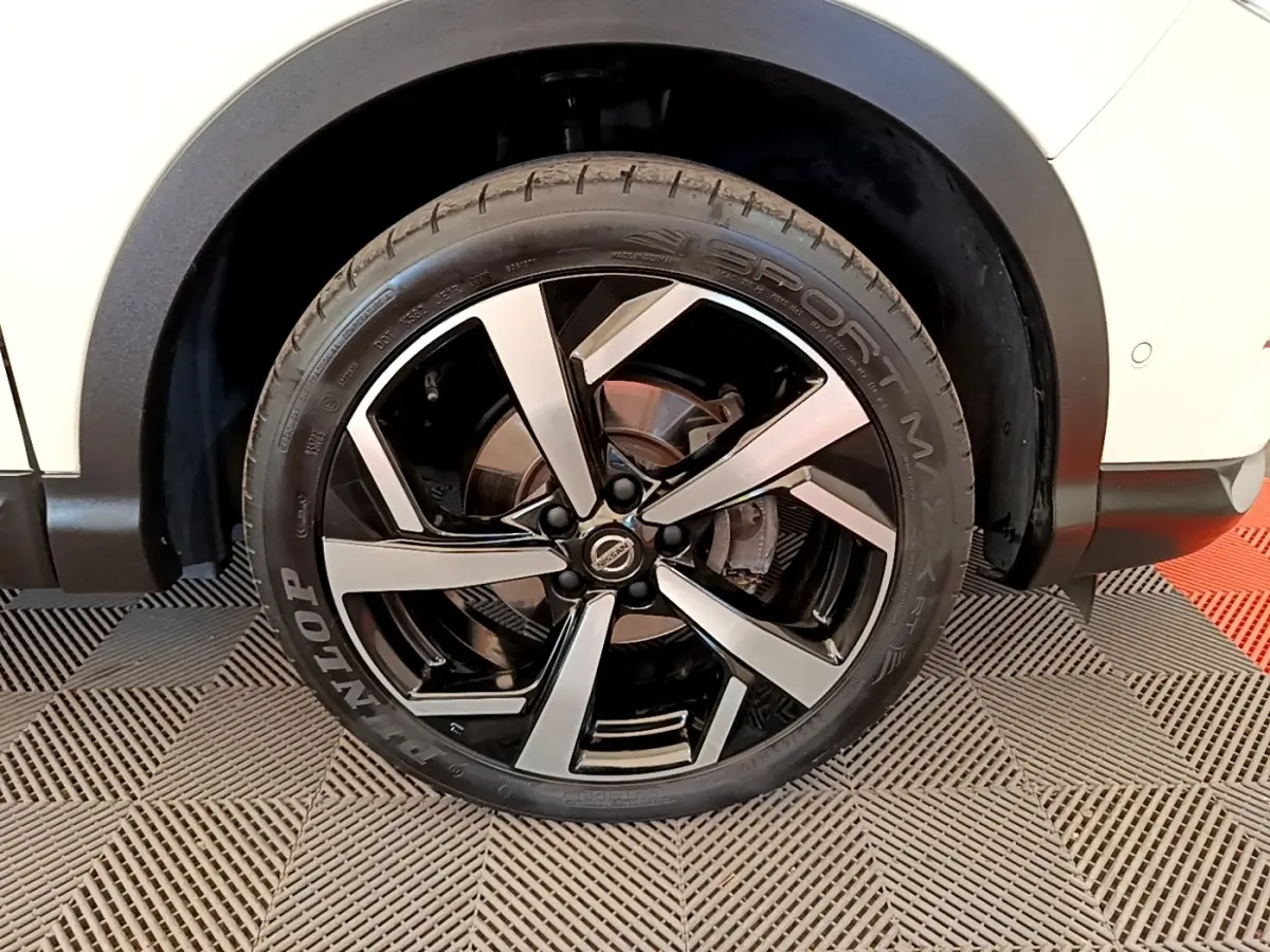 Gros plan sur la roue arrière droite d’un Nissan Qashqai blanc, mettant en valeur la jante alliage noire et argent.