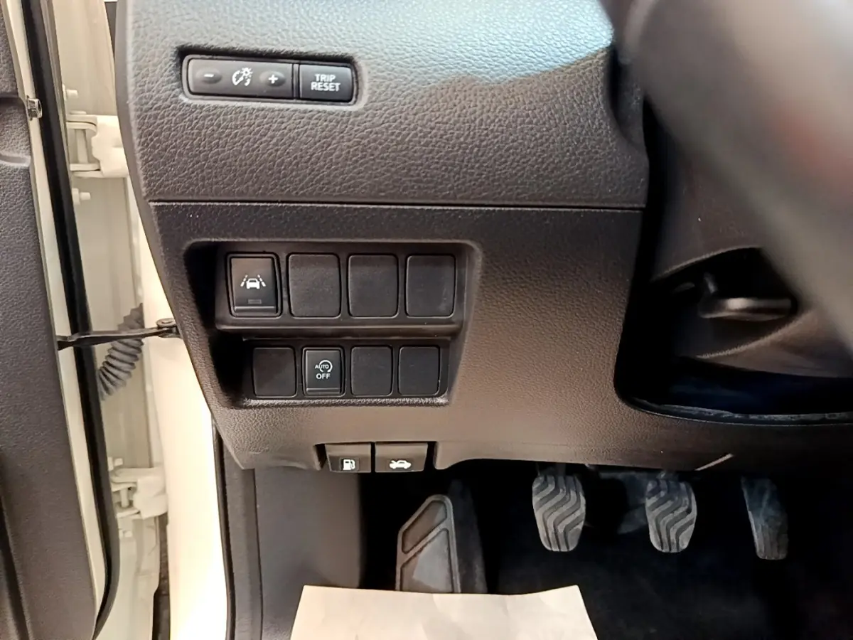Détail intérieur côté gauche du tableau de bord noir avec commandes et pédales du Nissan Qashqai blanc 2019.