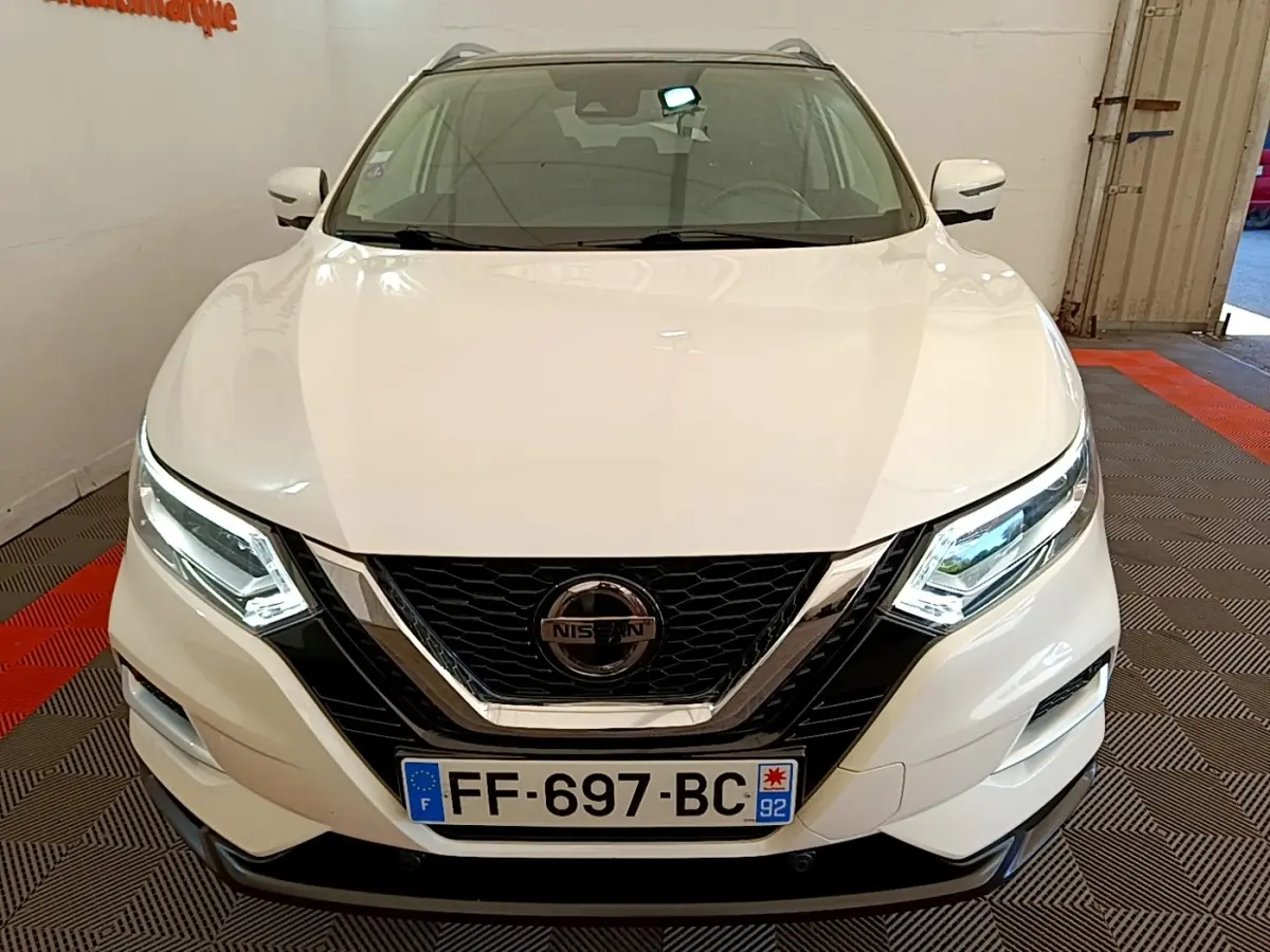 Vue avant d'un Nissan Qashqai blanc avec phares LED allumés et calandre noire chromée.