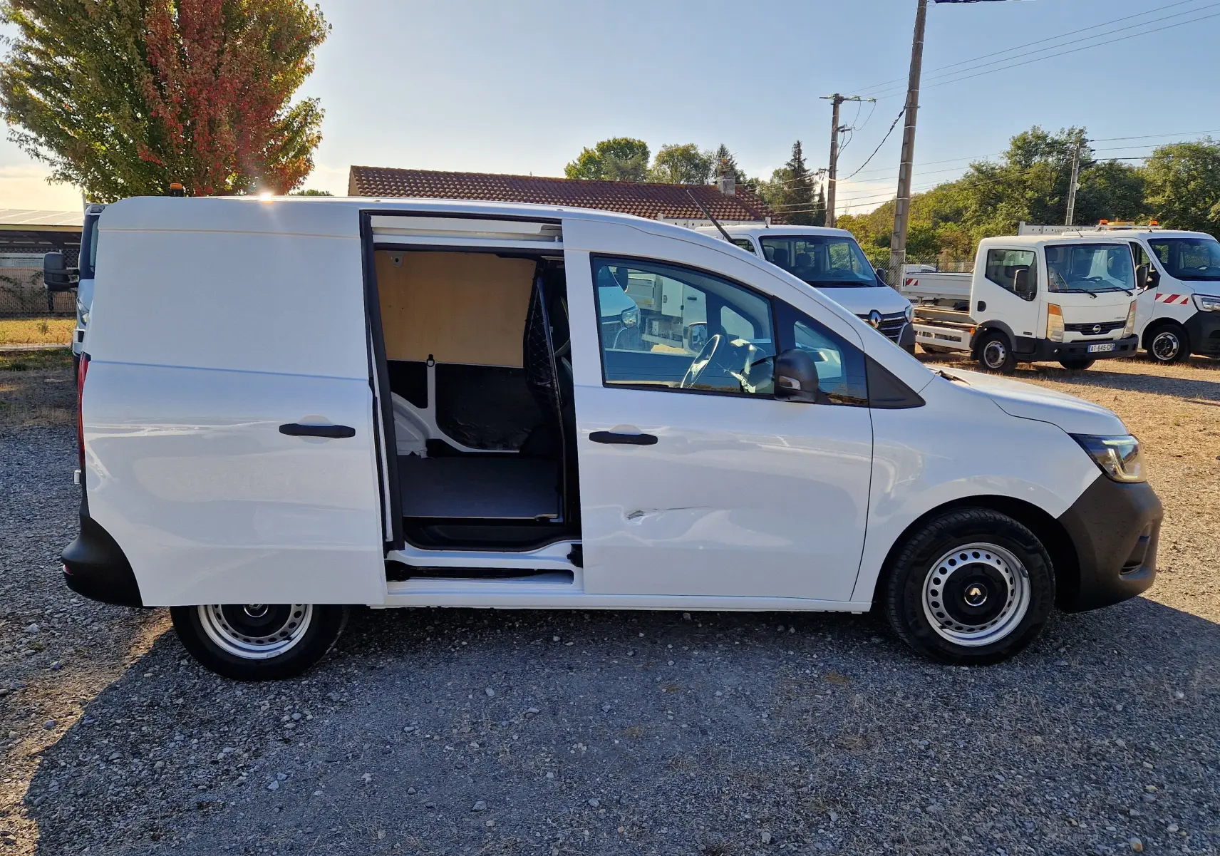 Vue latérale droite d’un Renault Kangoo blanc 2023 avec porte coulissante ouverte, montrant l’intérieur utilitaire et la grille de séparation.
