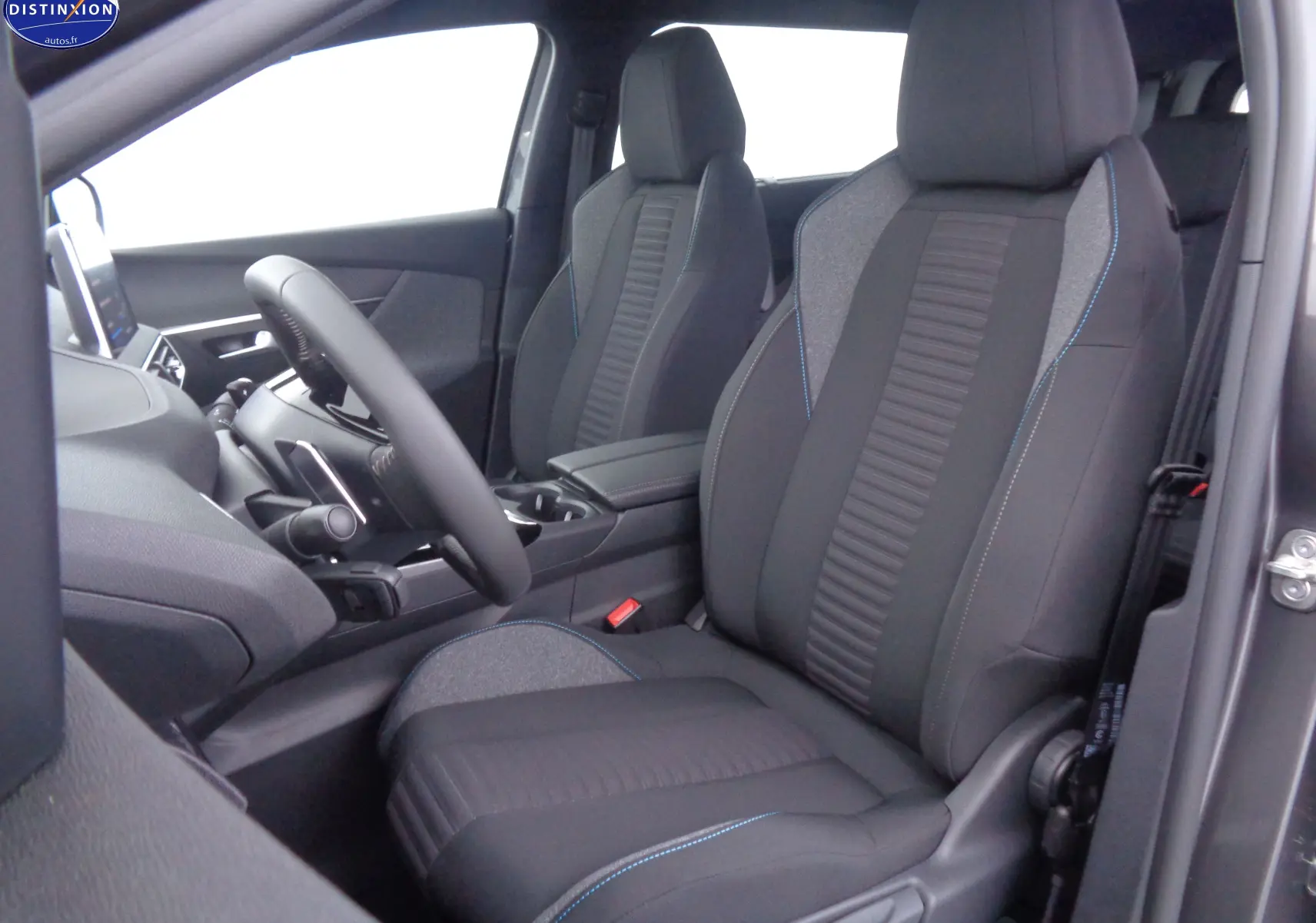Vue intérieure côté conducteur du Peugeot 5008 2023 avec sièges tissu noir et surpiqûres bleues, tableau de bord partiellement visible.