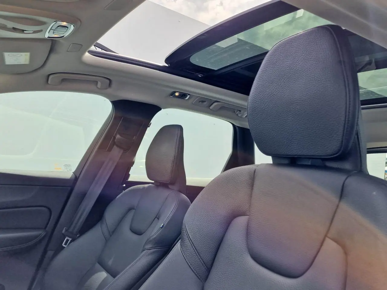 Intérieur du Volvo XC60 noir, vue sur sièges avant cuir et toit ouvrant panoramique lumineux.