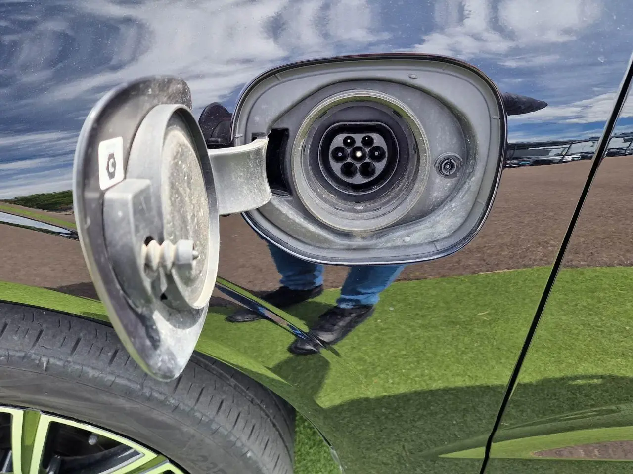 Prise de recharge ouverte côté gauche sur un Volvo XC60 noir, avec jante alliage visible en bas.