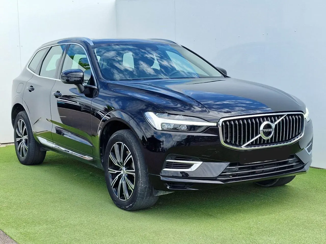 Volvo XC60 noir en 3/4 avant droit, avec calandre chromée et jantes alliage 19 pouces sur fond clair.