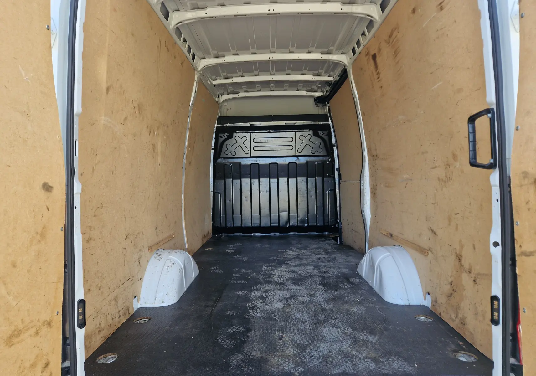 Intérieur du fourgon blanc Iveco Daily 2022 vu de l'arrière, avec parois en bois et plancher noir usé.