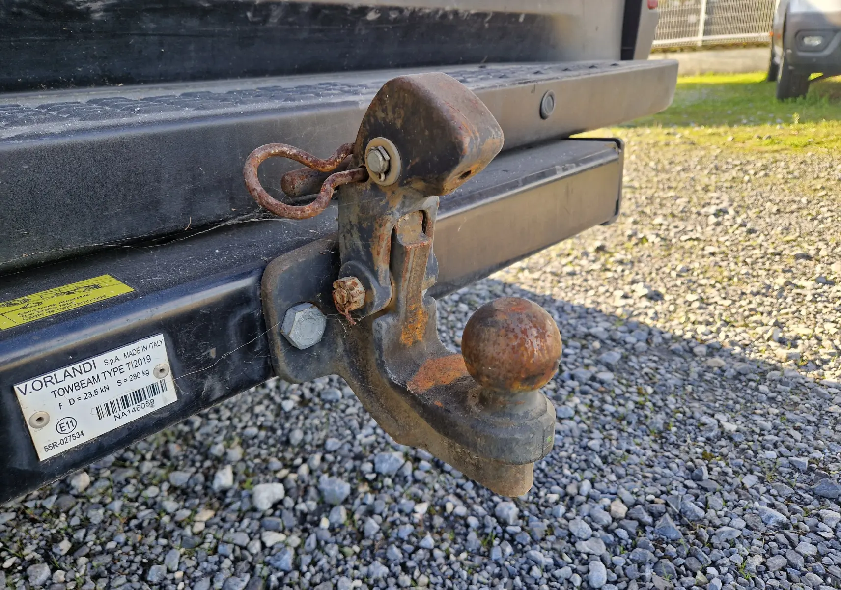 Gros plan sur l'attelage rouillé fixé à l'arrière du fourgon blanc Iveco Daily 2022, sur un sol gravillonné.