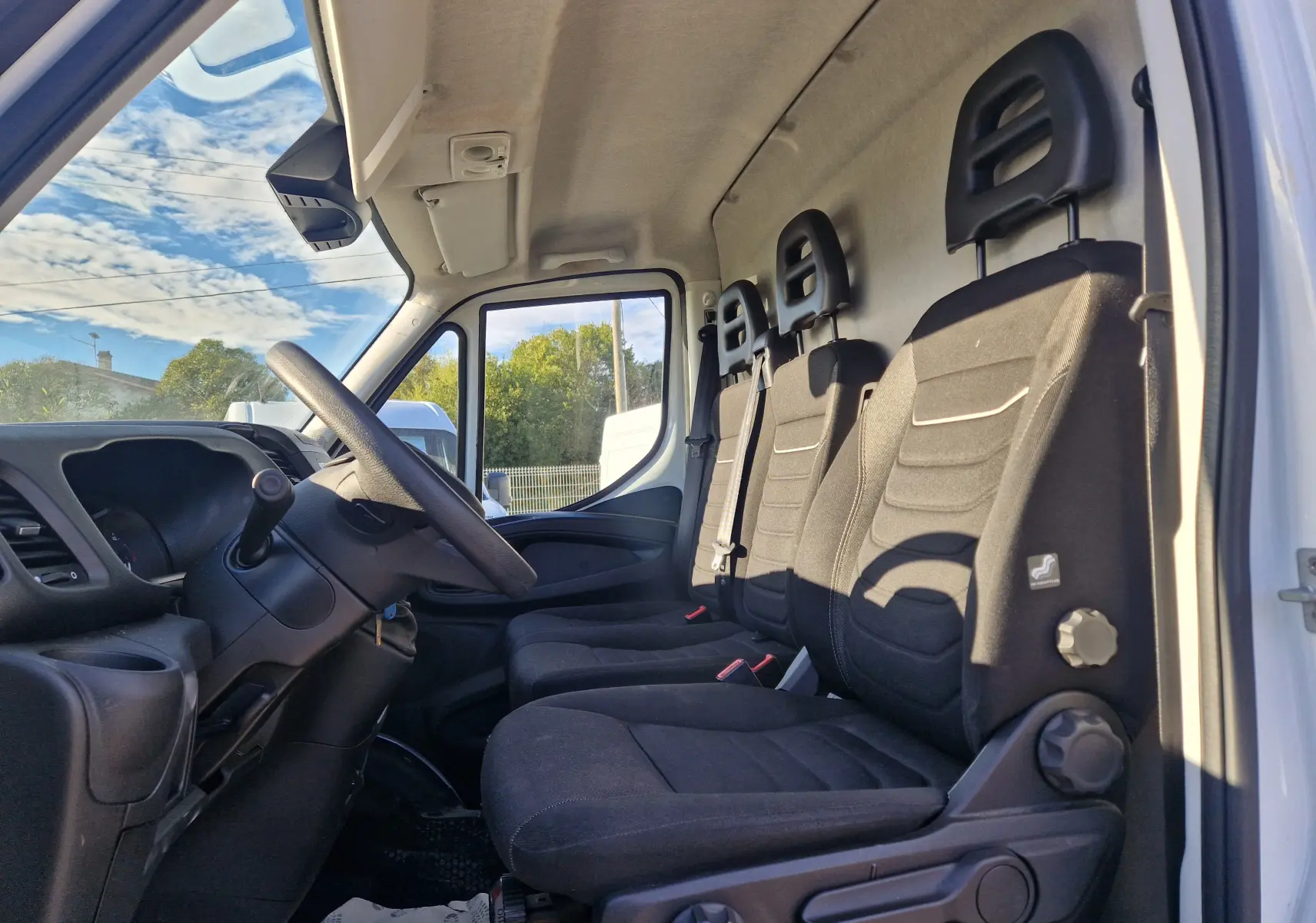 Vue intérieure côté conducteur du fourgon blanc Iveco Daily 2022, montrant les sièges noirs et le volant multifonction.