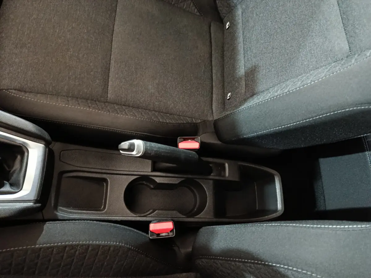 Vue plongeante sur la console centrale noire entre les sièges avant tissu gris de la Renault Clio Business blanche 2021.