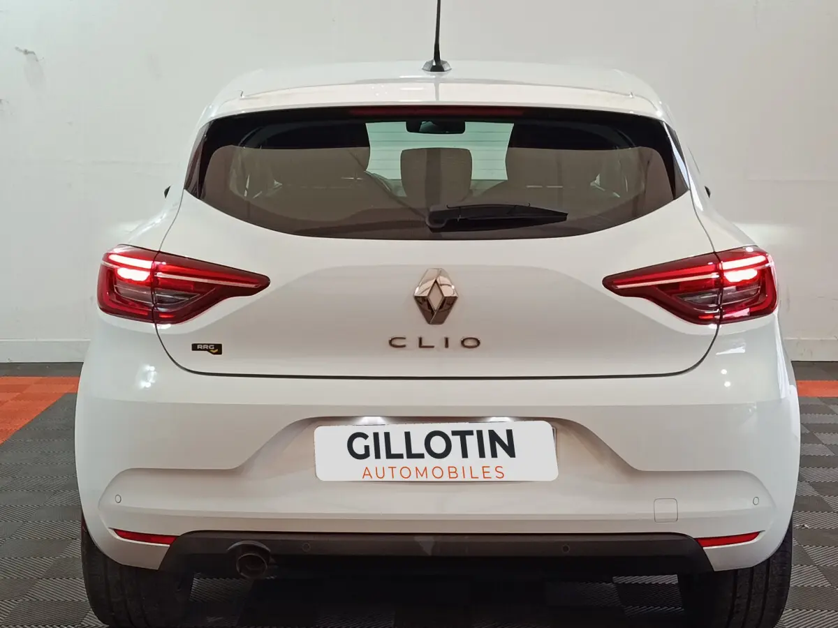 Vue arrière d'une Renault Clio blanche 2021 avec feux LED allumés et logo central visible.