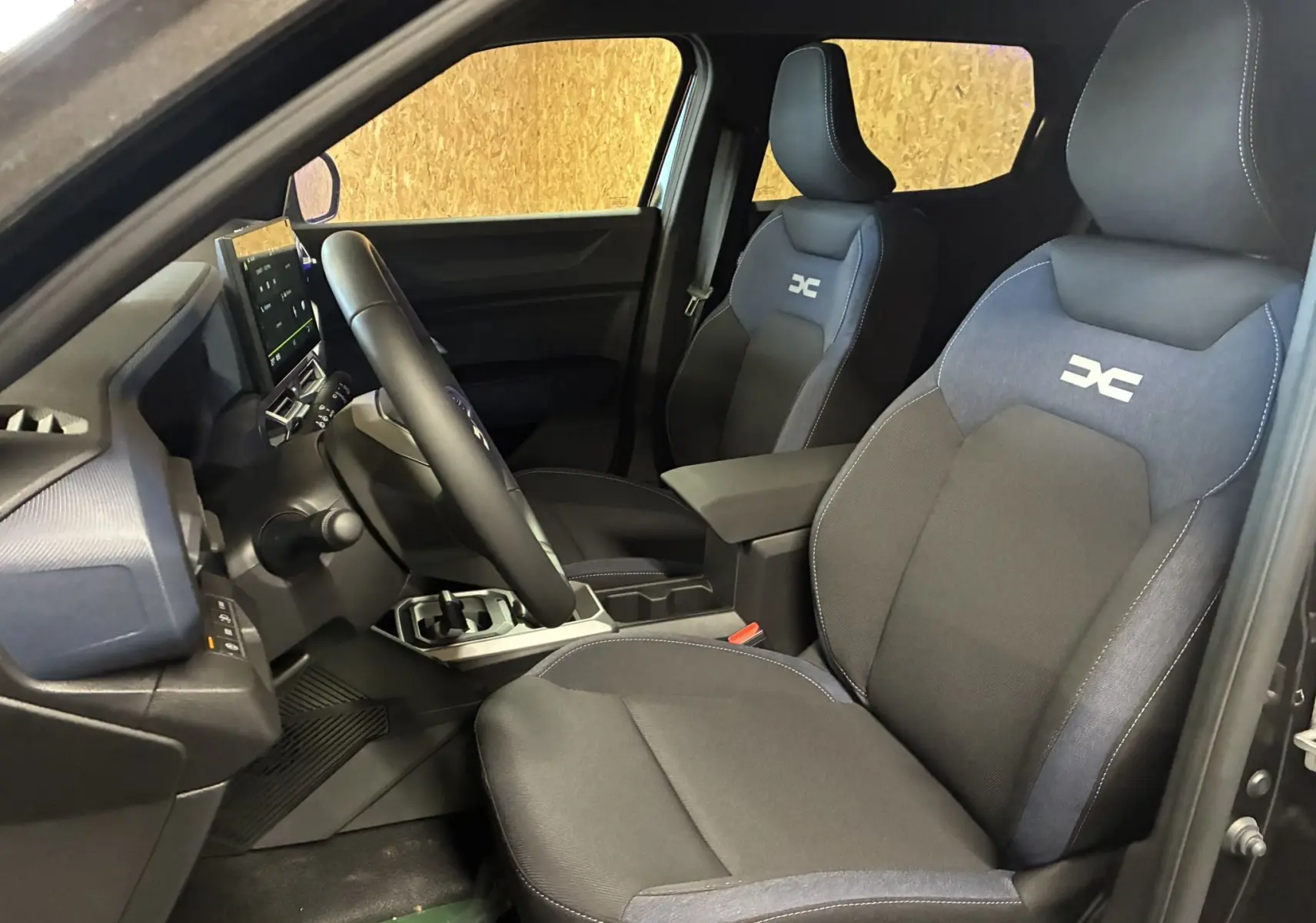 Vue intérieure côté conducteur du Dacia Duster 1.6 Hybrid 140 Journey noir, sièges tissu gris-noir avec logo distinctif brodé.
