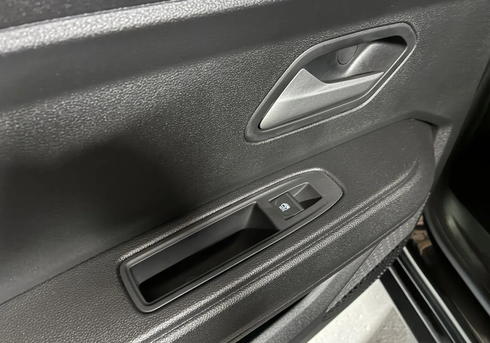 Gros plan sur la poignée intérieure et le bouton de commande de vitre électrique côté porte avant gauche du Dacia Duster noir 2025.