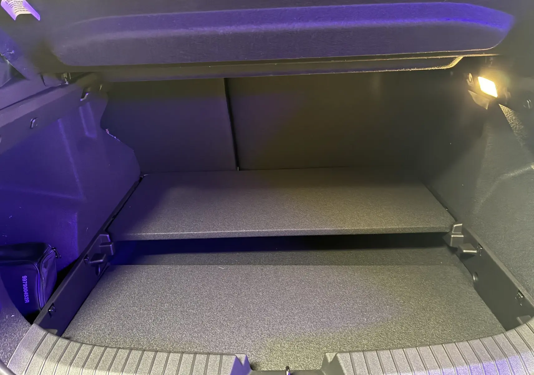 Coffre ouvert du Dacia Duster 1.6 Hybrid 140 Journey 2025 noir, vue intérieure montrant le double plancher et l'éclairage latéral.