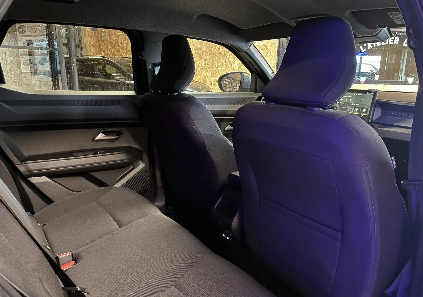 Vue intérieure arrière du Dacia Duster 1.6 Hybrid 140 Journey 2025 noir, sièges tissu gris foncé et tableau de bord visible.