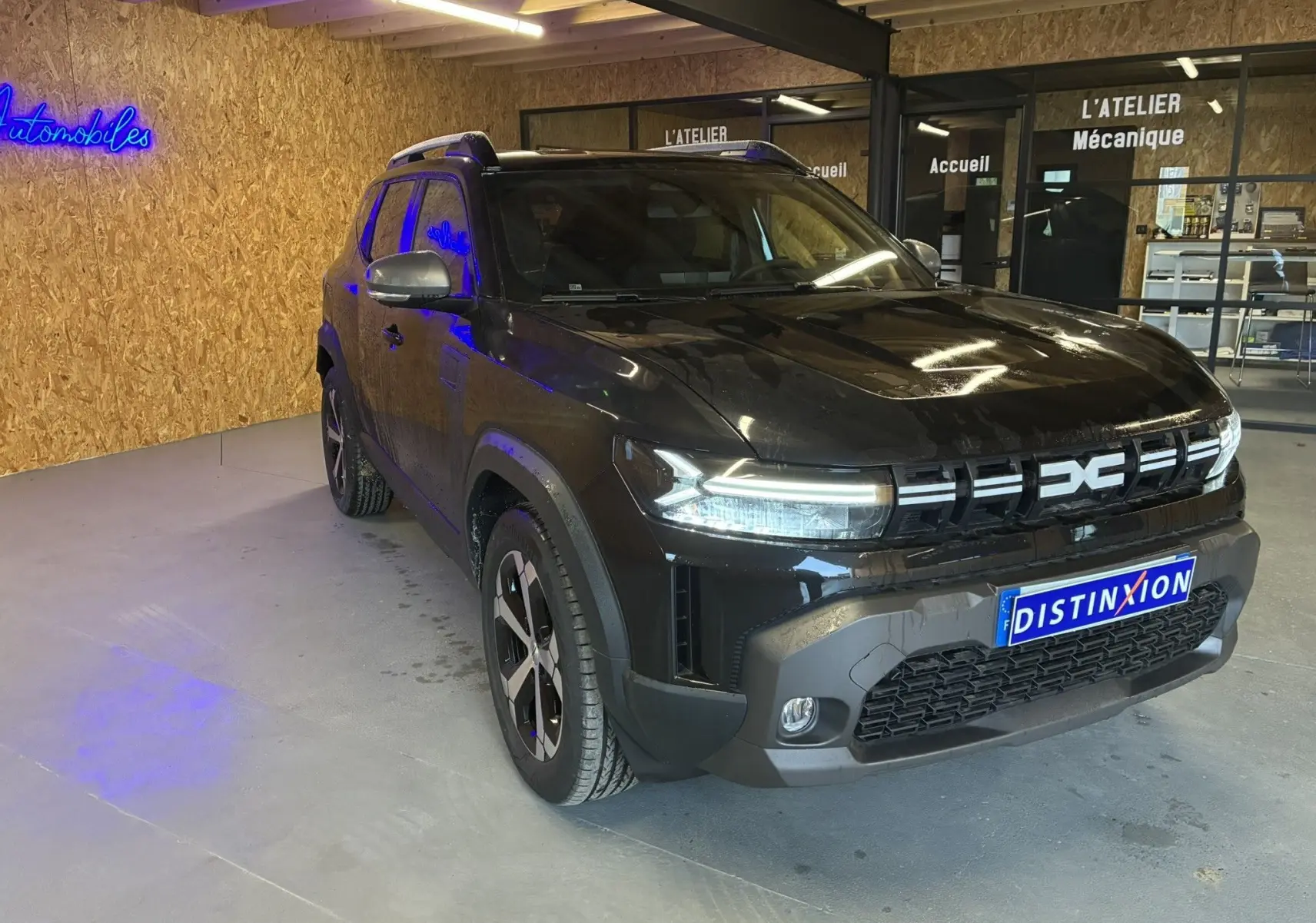 Vue 3/4 avant d'un Dacia Duster 1.6 Hybrid 140 noir, avec calandre distinctive et jantes noires, en intérieur d'atelier.