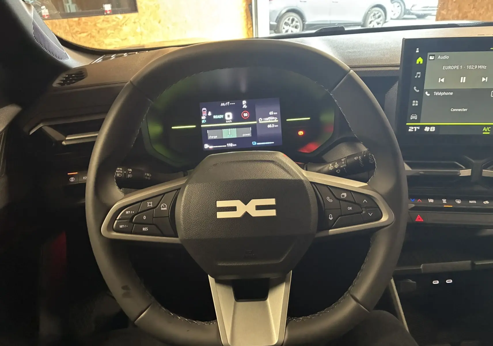 Vue intérieure centrée sur le volant noir du Dacia Duster 1.6 Hybrid 140 avec tableau de bord numérique et écran tactile.