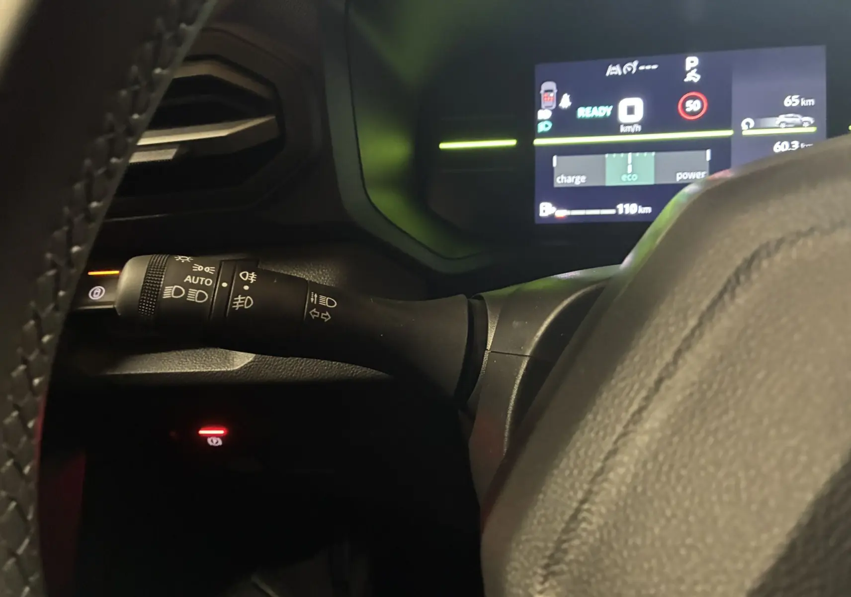 Vue rapprochée du commodo d’éclairage noir à gauche du volant dans un Dacia Duster 2025 avec tableau de bord numérique allumé.