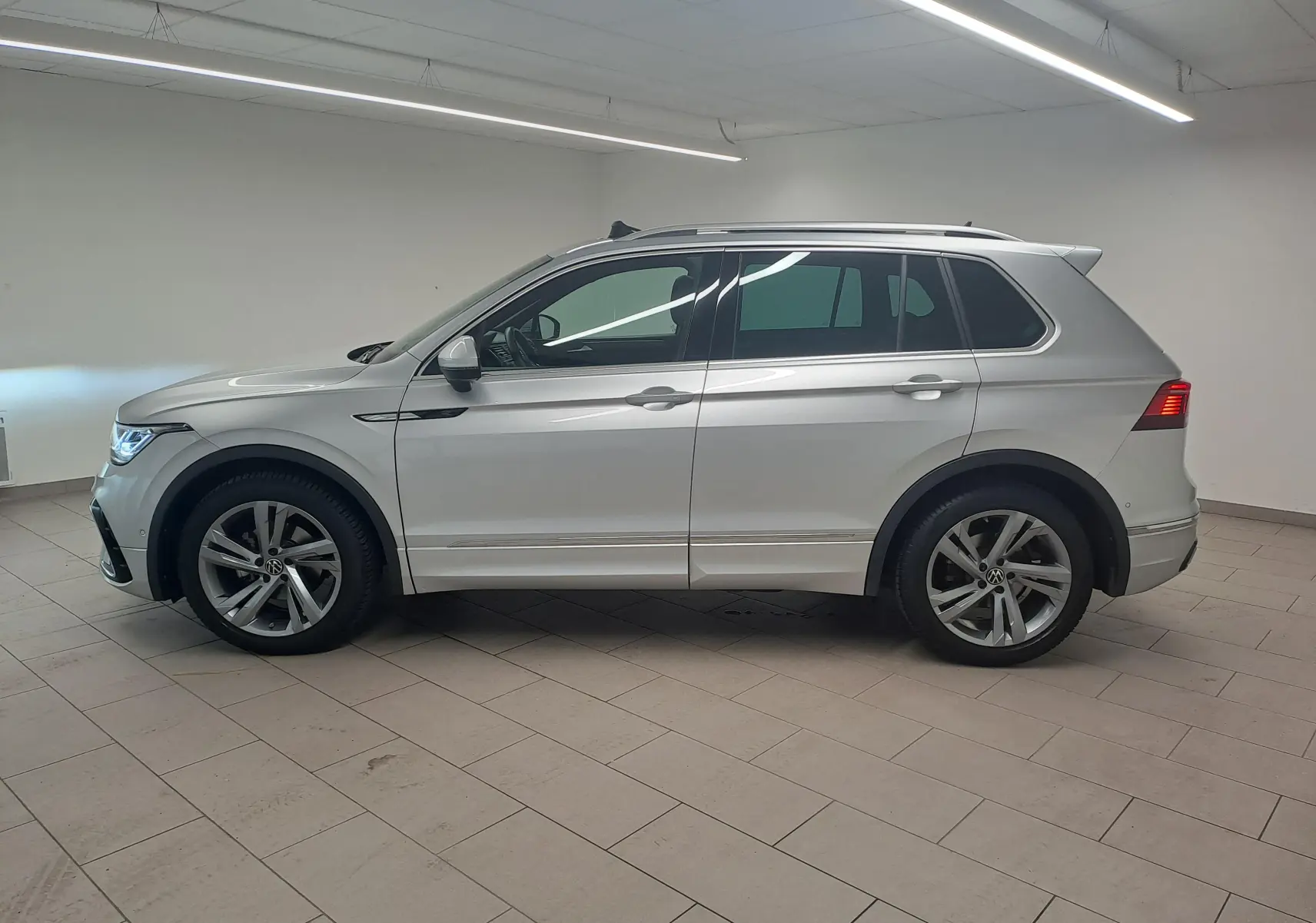 Vue de profil côté gauche du Volkswagen Tiguan 2024 en peinture métallisée Reflet d'Argent, avec jantes alliage et attelage escamotable.