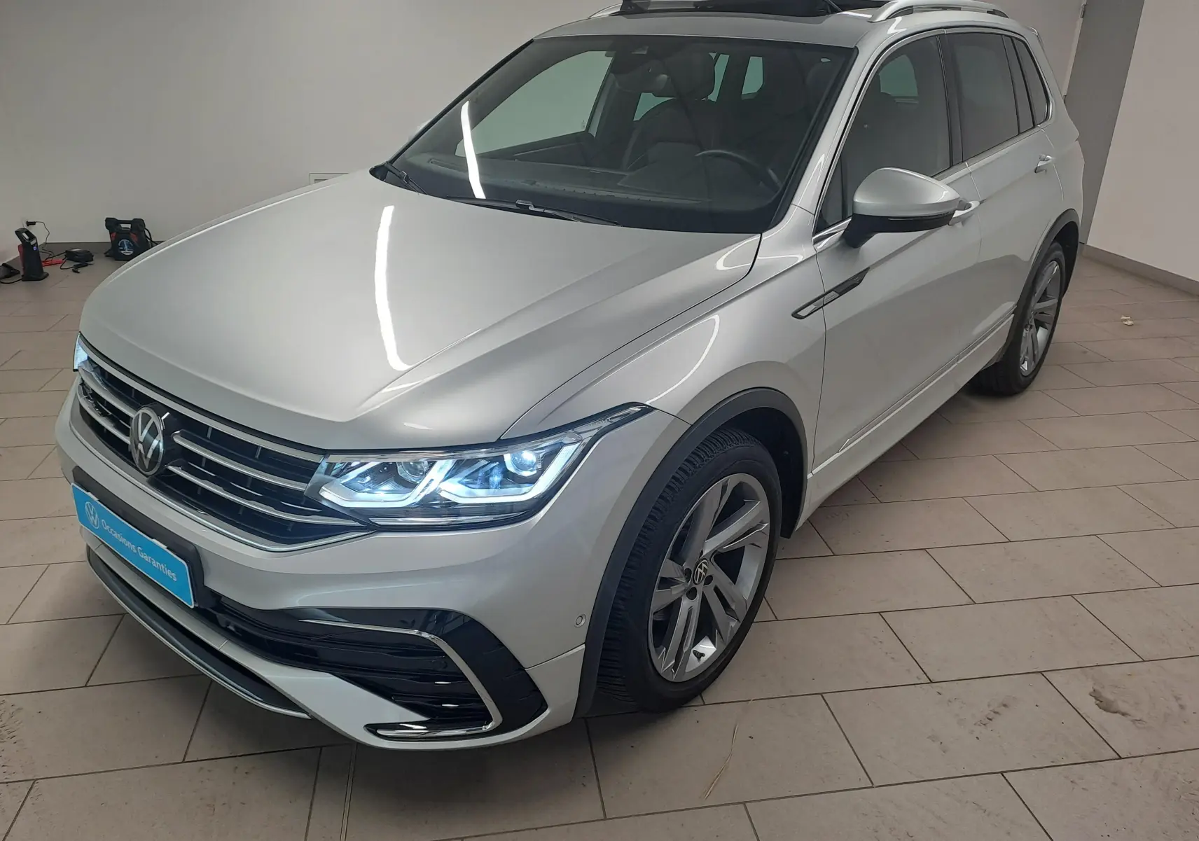 Vue 3/4 avant droite d’un Volkswagen Tiguan 2024 argent métallisé avec phares LED allumés et jantes alliage R-Line.