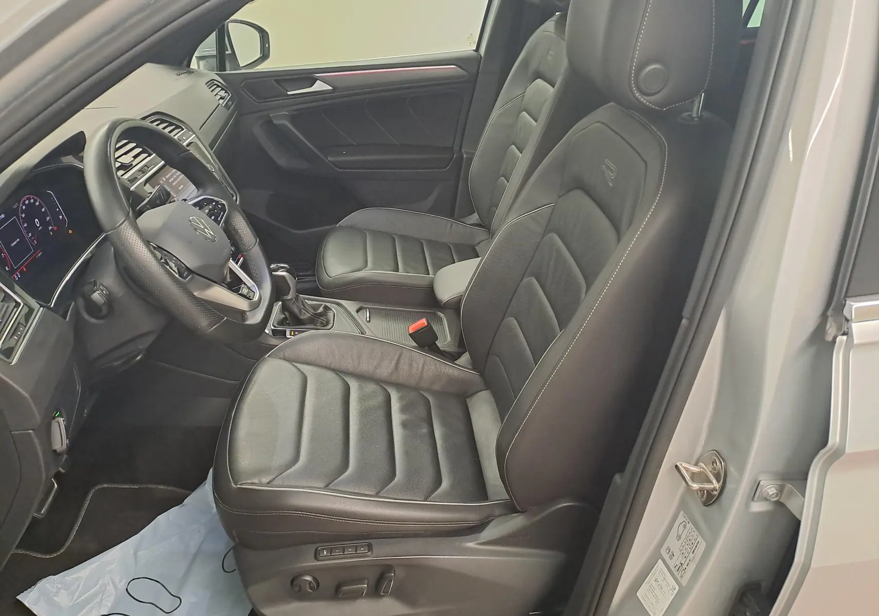 Vue intérieure côté gauche du Volkswagen Tiguan 2024 argent, avec sièges avant en cuir noir et volant multifonction.