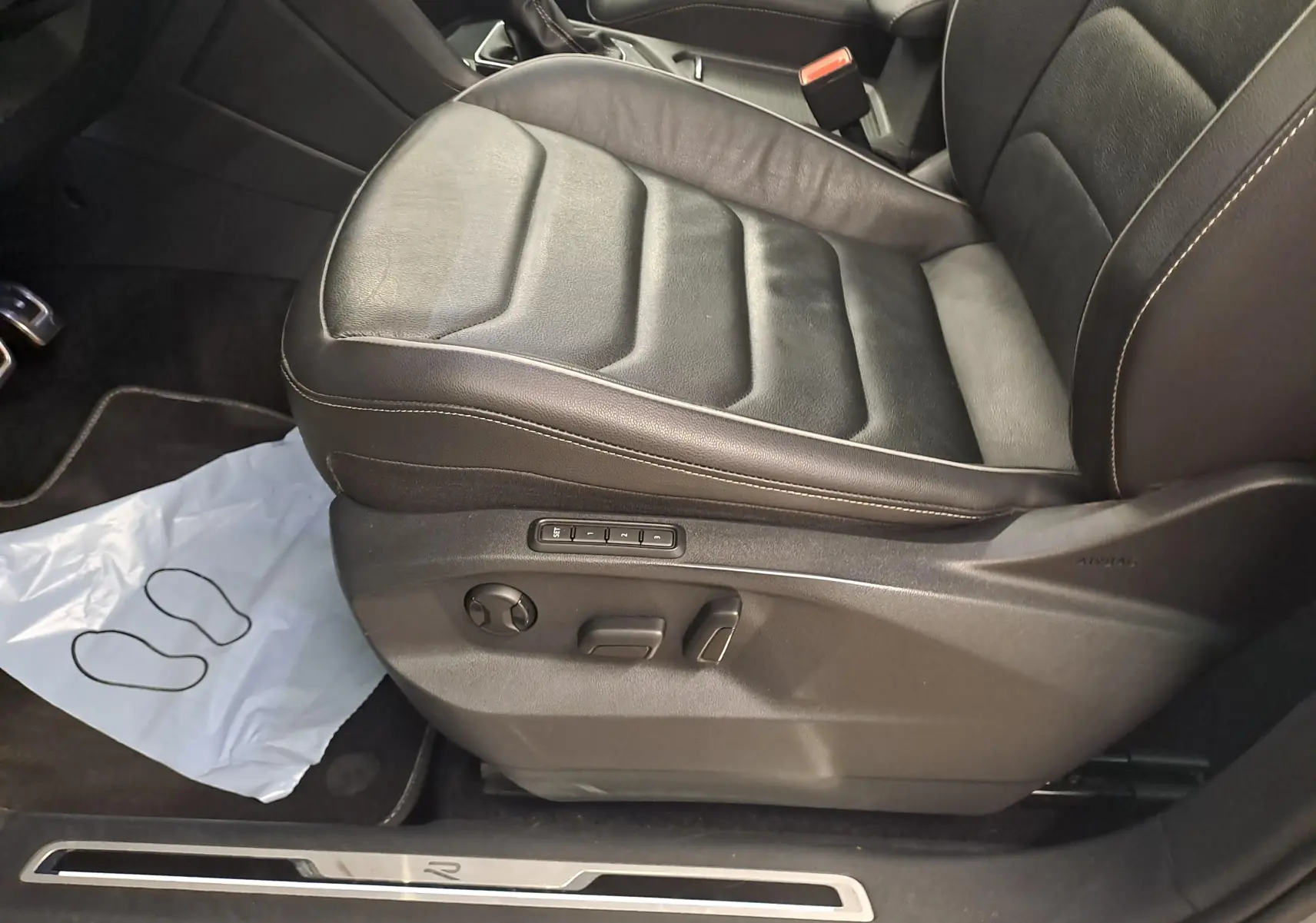 Vue rapprochée du siège avant gauche en cuir noir du Volkswagen Tiguan 2024, avec réglages électriques et surpiqûres claires.