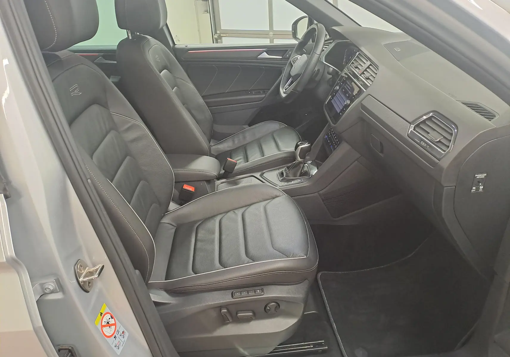 Vue intérieure côté conducteur du Volkswagen Tiguan 2024 argent, sièges cuir noirs R-Line avec commandes électriques.