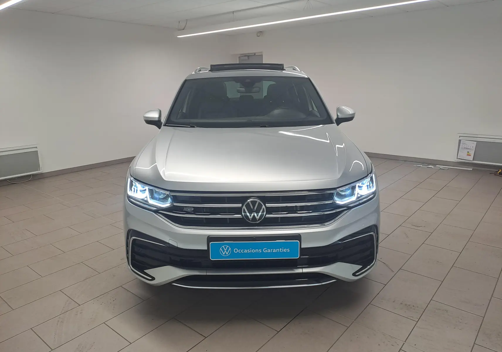 Vue frontale d'un Volkswagen Tiguan 2024 gris Reflet d'Argent avec phares LED allumés et calandre R-Line.