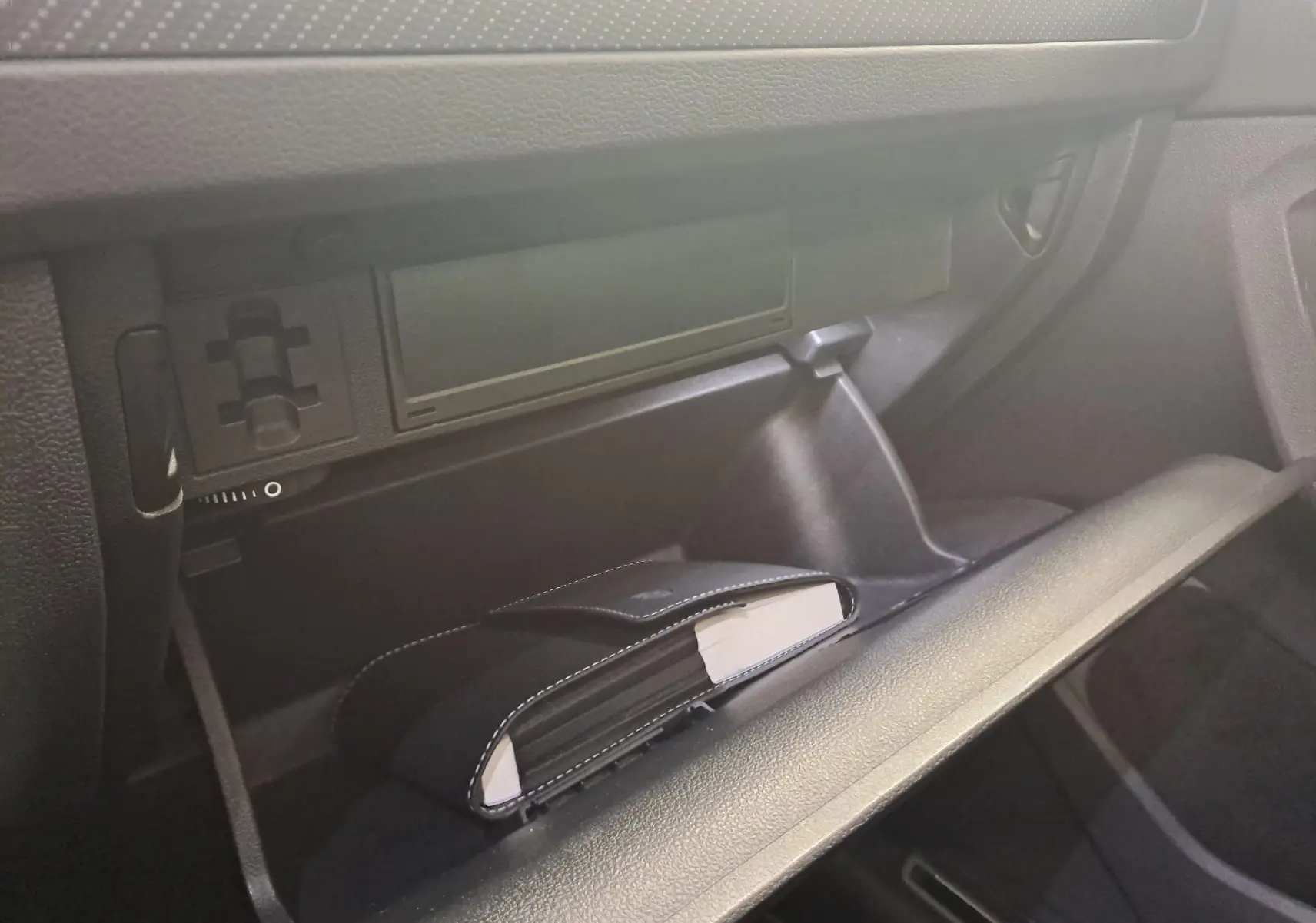 Gros plan de la boîte à gants ouverte du Volkswagen Tiguan 2024, avec un carnet noir à l'intérieur, intérieur noir.