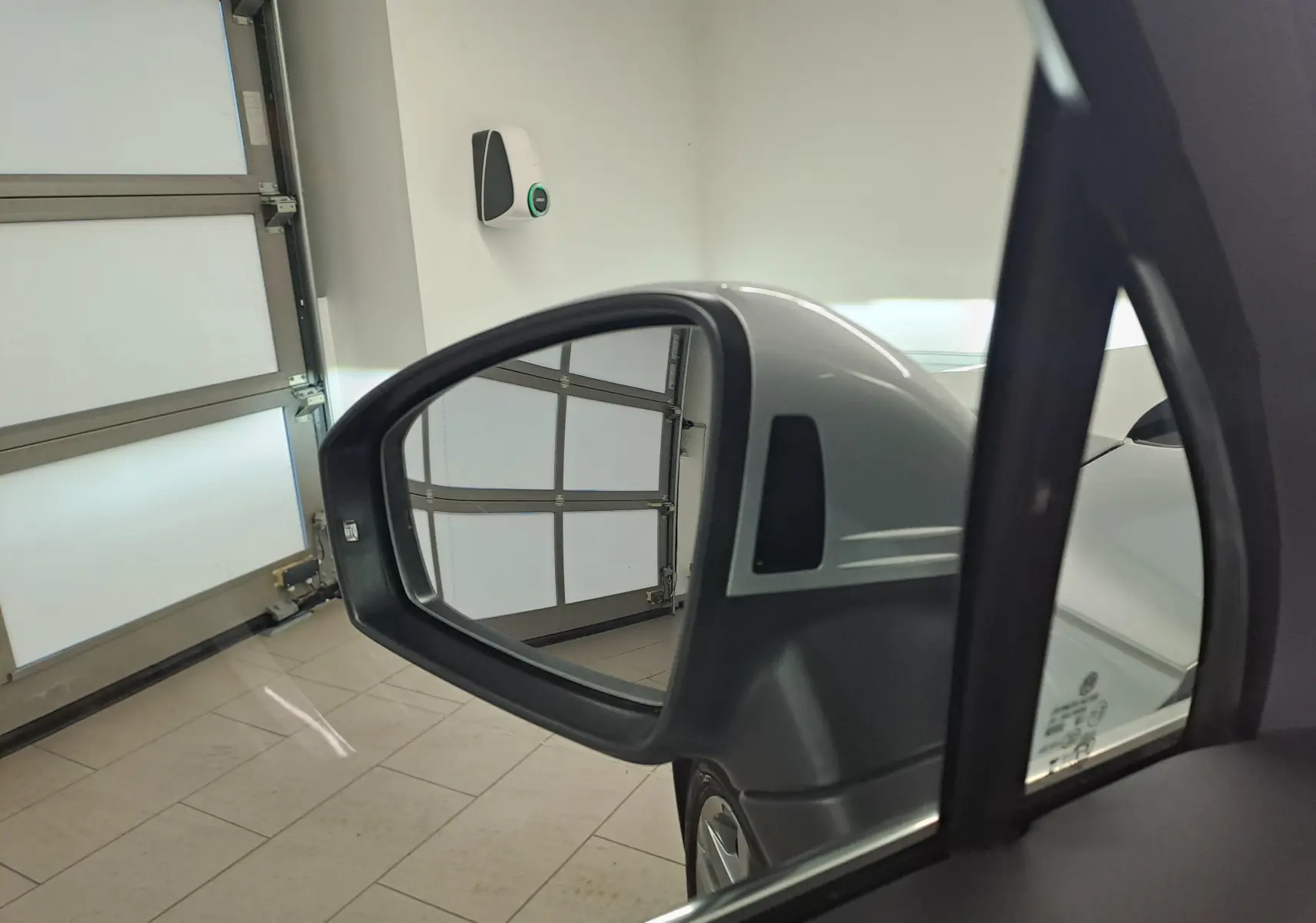 Rétroviseur côté gauche d'un Volkswagen Tiguan 2024 argenté, avec reflet de porte de garage en arrière-plan.