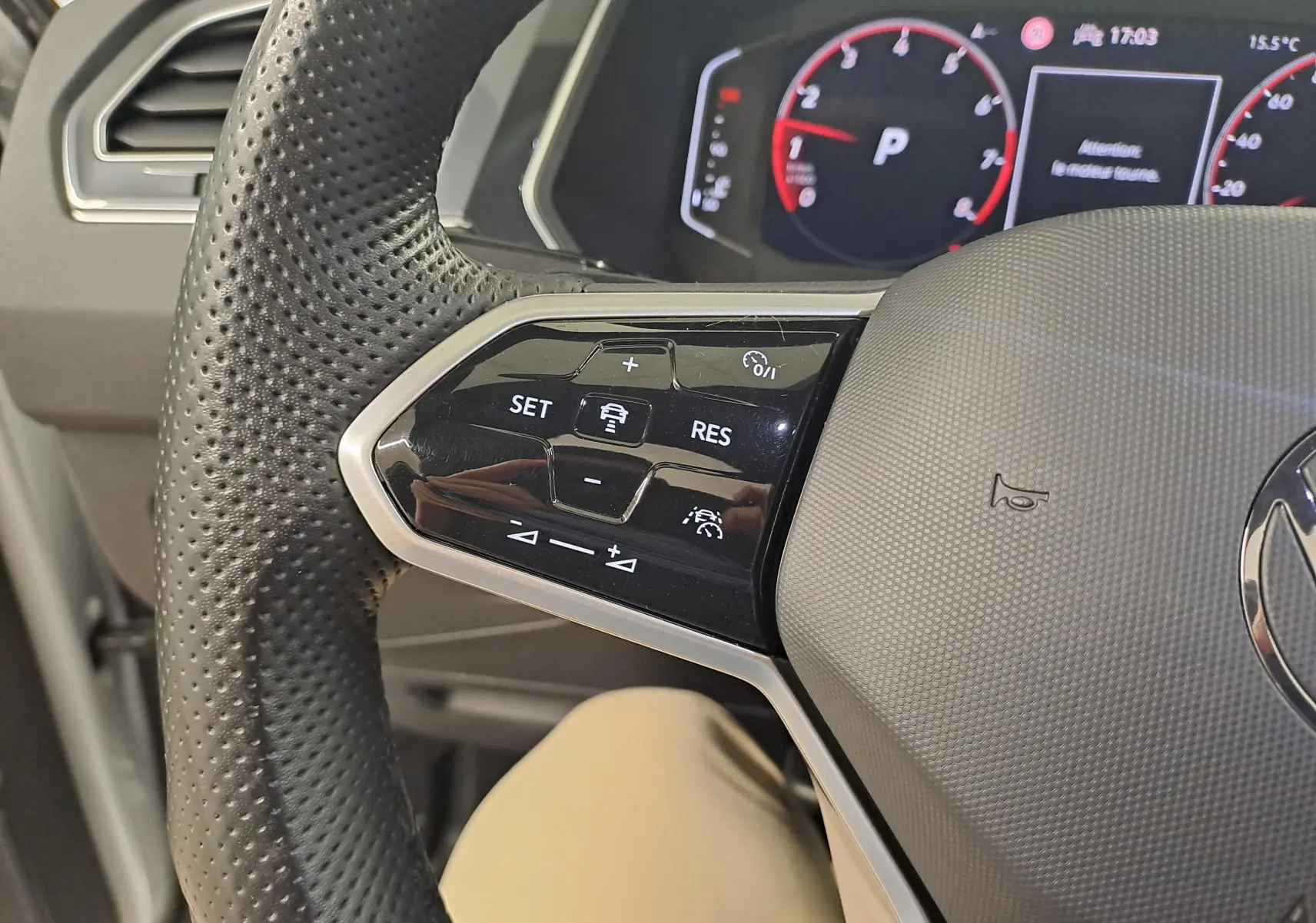 Gros plan sur le volant perforé du Volkswagen Tiguan 2024, avec commandes de régulateur et tableau de bord numérique en arrière-plan.