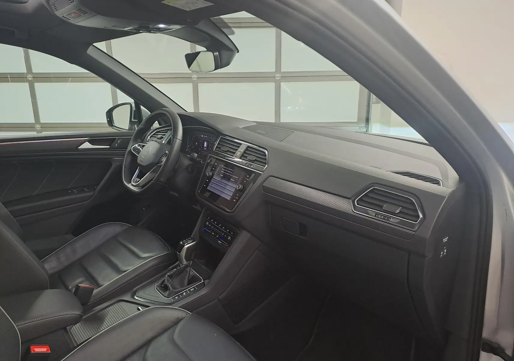Vue intérieure côté conducteur du Volkswagen Tiguan 2024 en Reflet d'Argent, avec tableau de bord et volant multifonction.