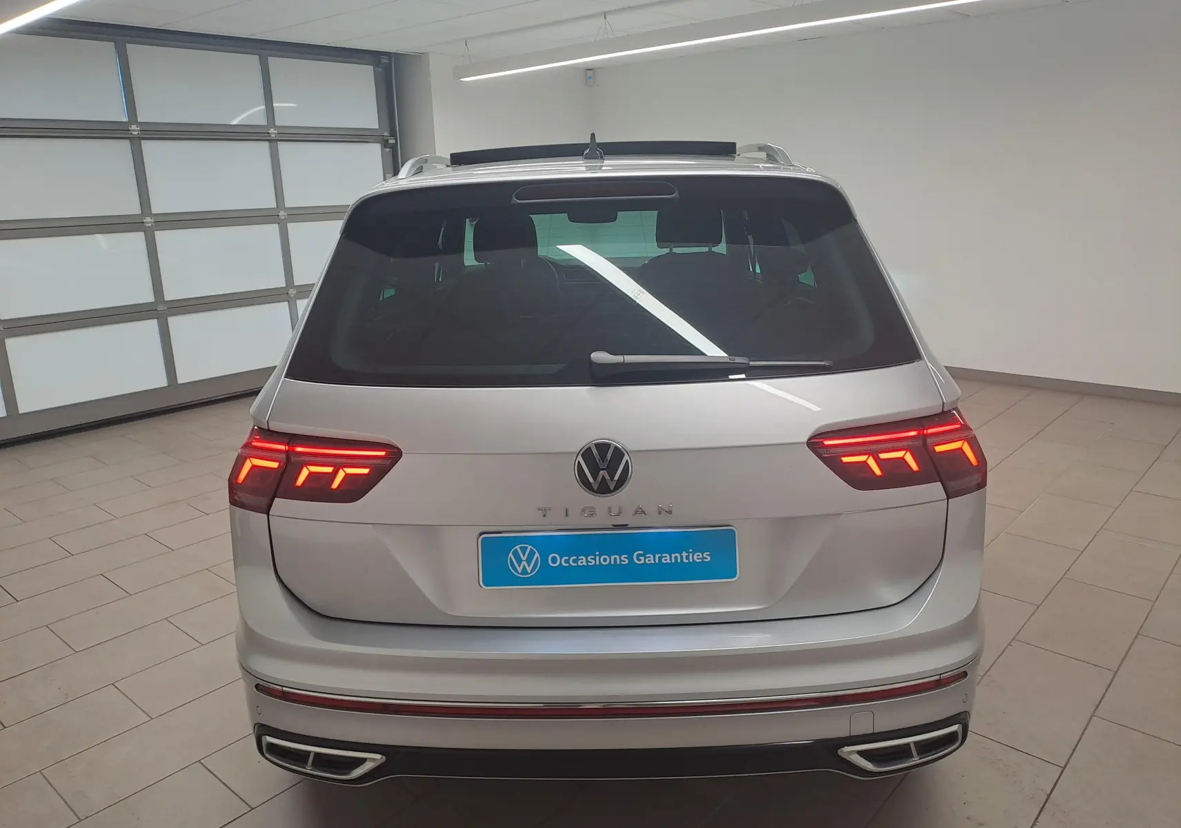 Vue arrière d'un Volkswagen Tiguan 2024 gris Reflet d'Argent avec feux LED allumés et attelage escamotable visible.
