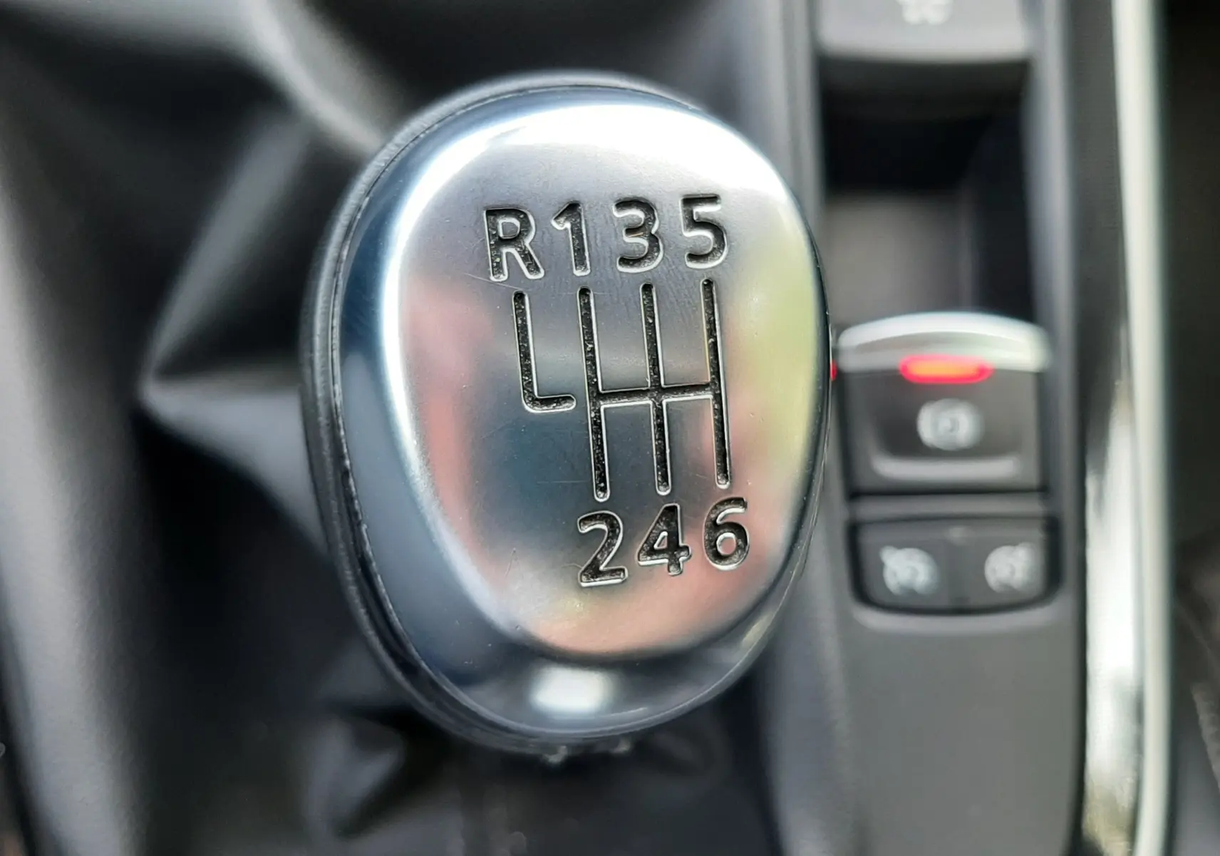 Gros plan sur le levier de vitesses manuel chromé du Renault Scénic IV gris Cassiopée, avec commandes électroniques en arrière-plan.