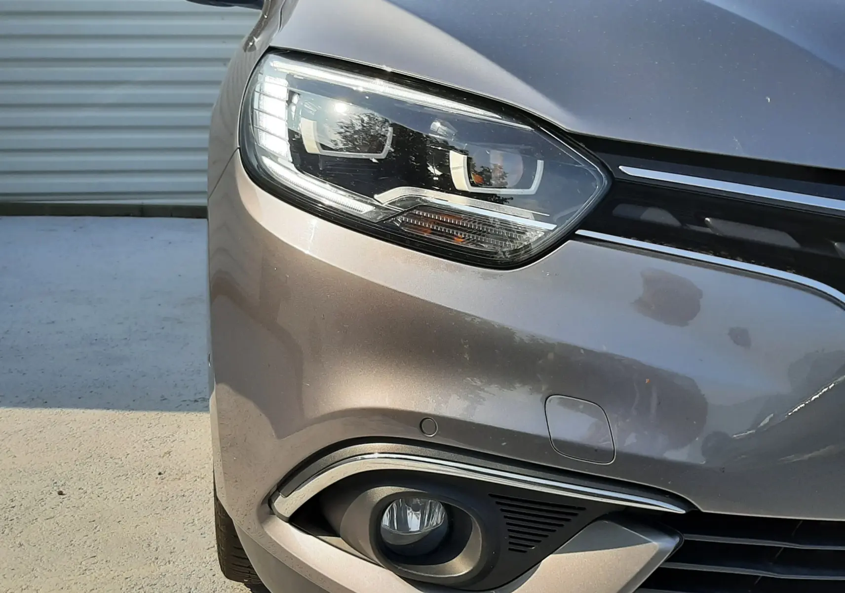 Gros plan sur l'avant gauche du Renault Scenic IV gris Cassiopée avec phare LED et antibrouillard intégré.