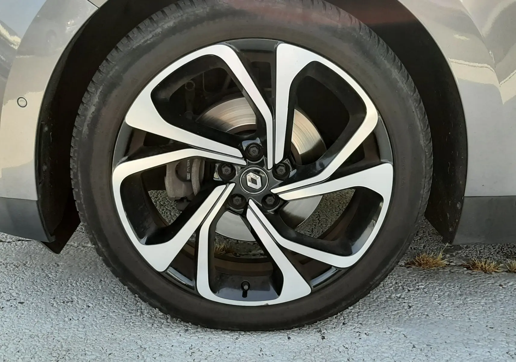 Gros plan sur la roue avant gauche du Renault Scénic IV gris Cassiopée, jante alliage noir et argentée au design moderne.