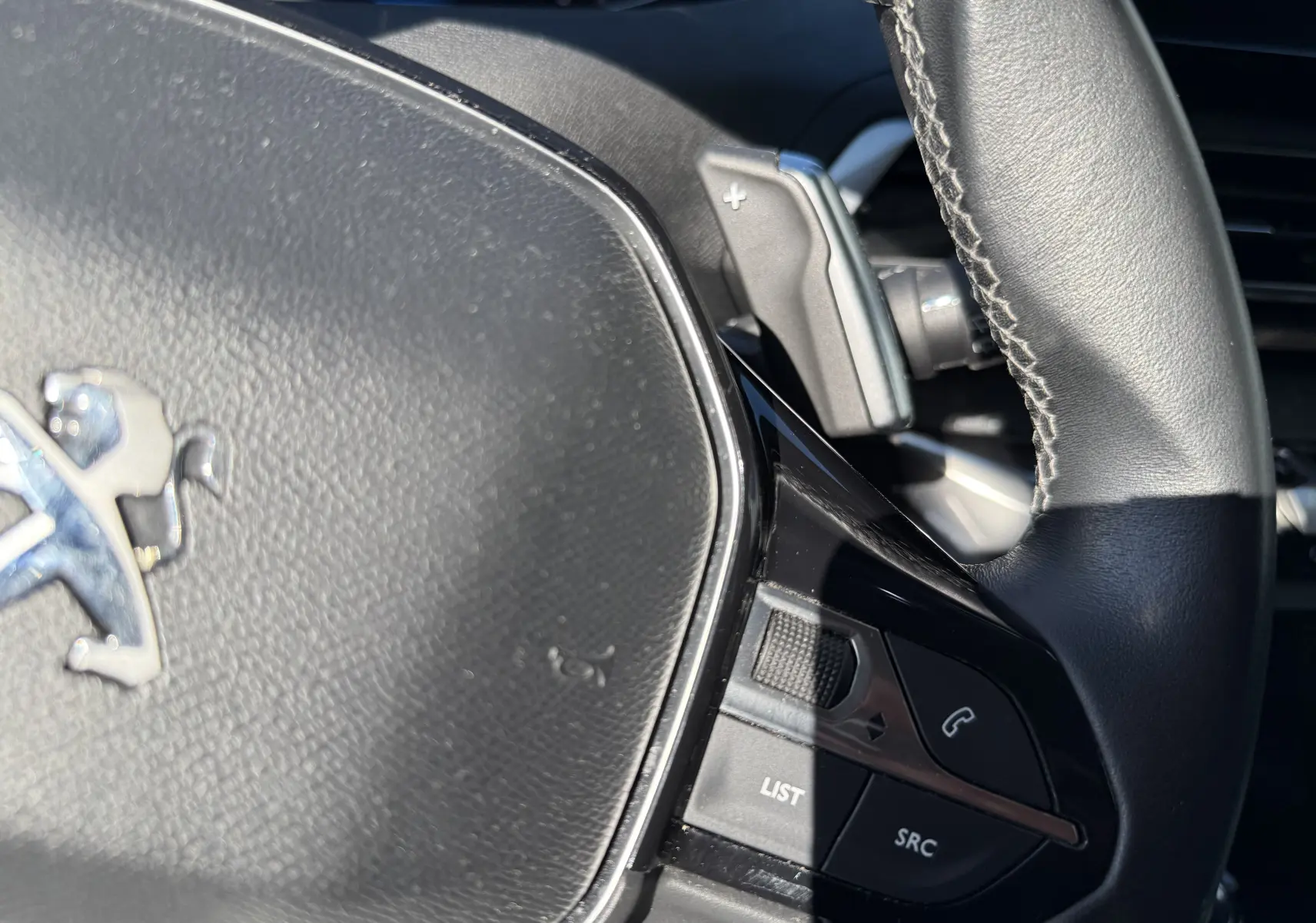 Gros plan sur le volant noir du Peugeot 5008 1.5 HDI 130 Allure, avec commandes audio et palette de changement de vitesse.