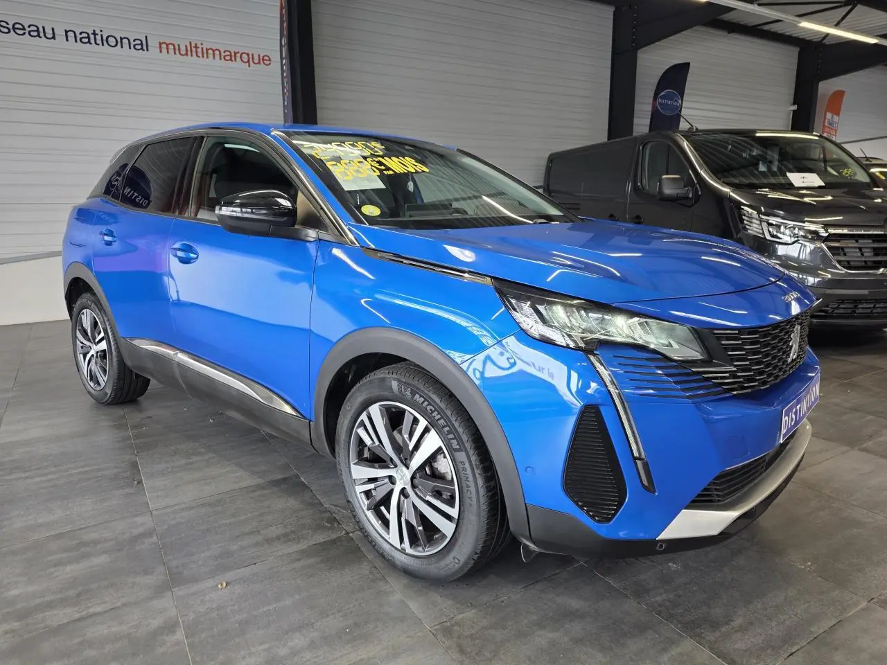 Peugeot 3008 Bleu Iron en 3/4 avant droit, avec jantes alliage bi-ton et calandre chromée dans un showroom.