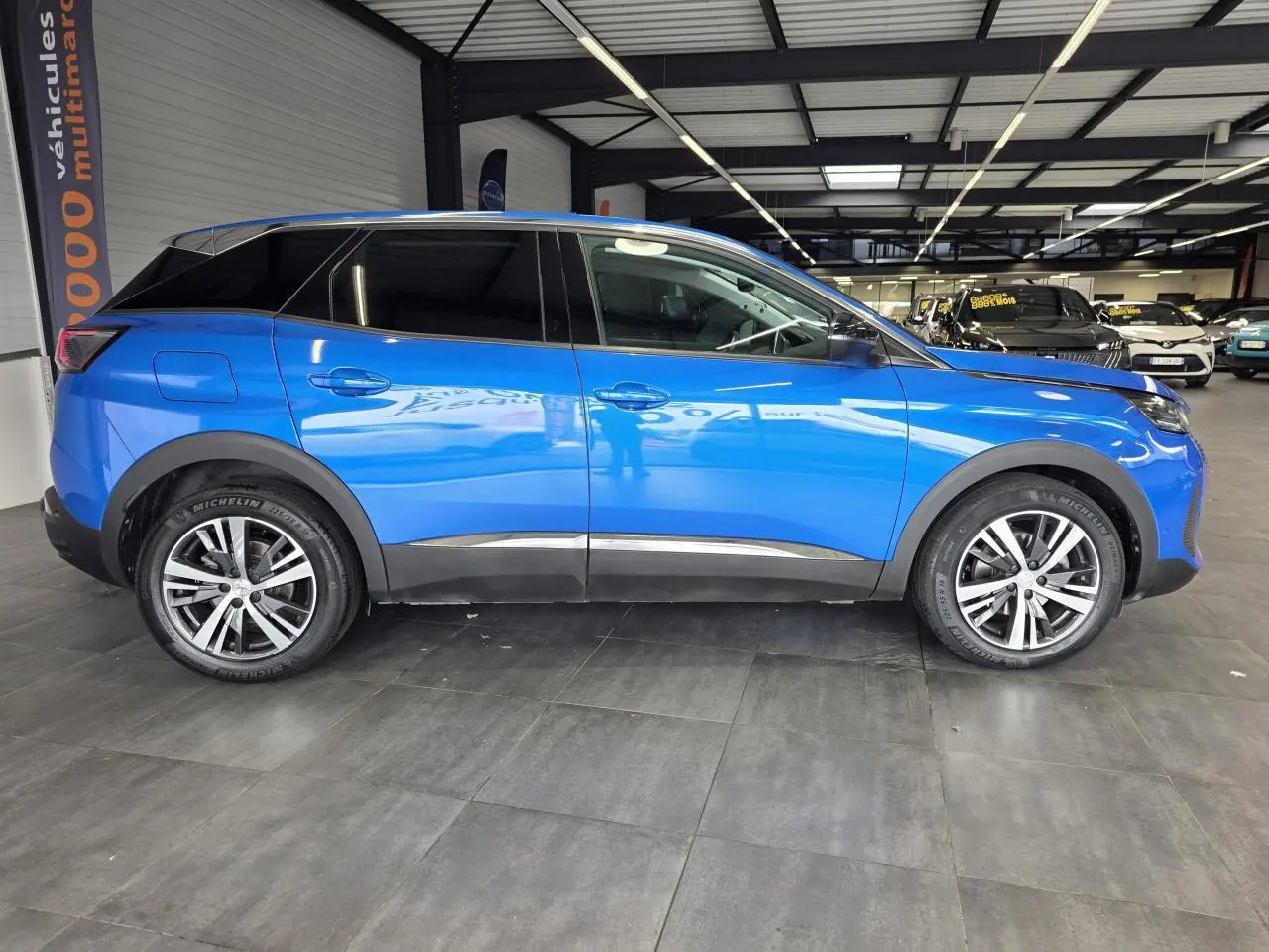 Profil droit d'un Peugeot 3008 bleu Iron métallisé avec jantes alliage bi-ton et vitres surteintées en intérieur showroom.