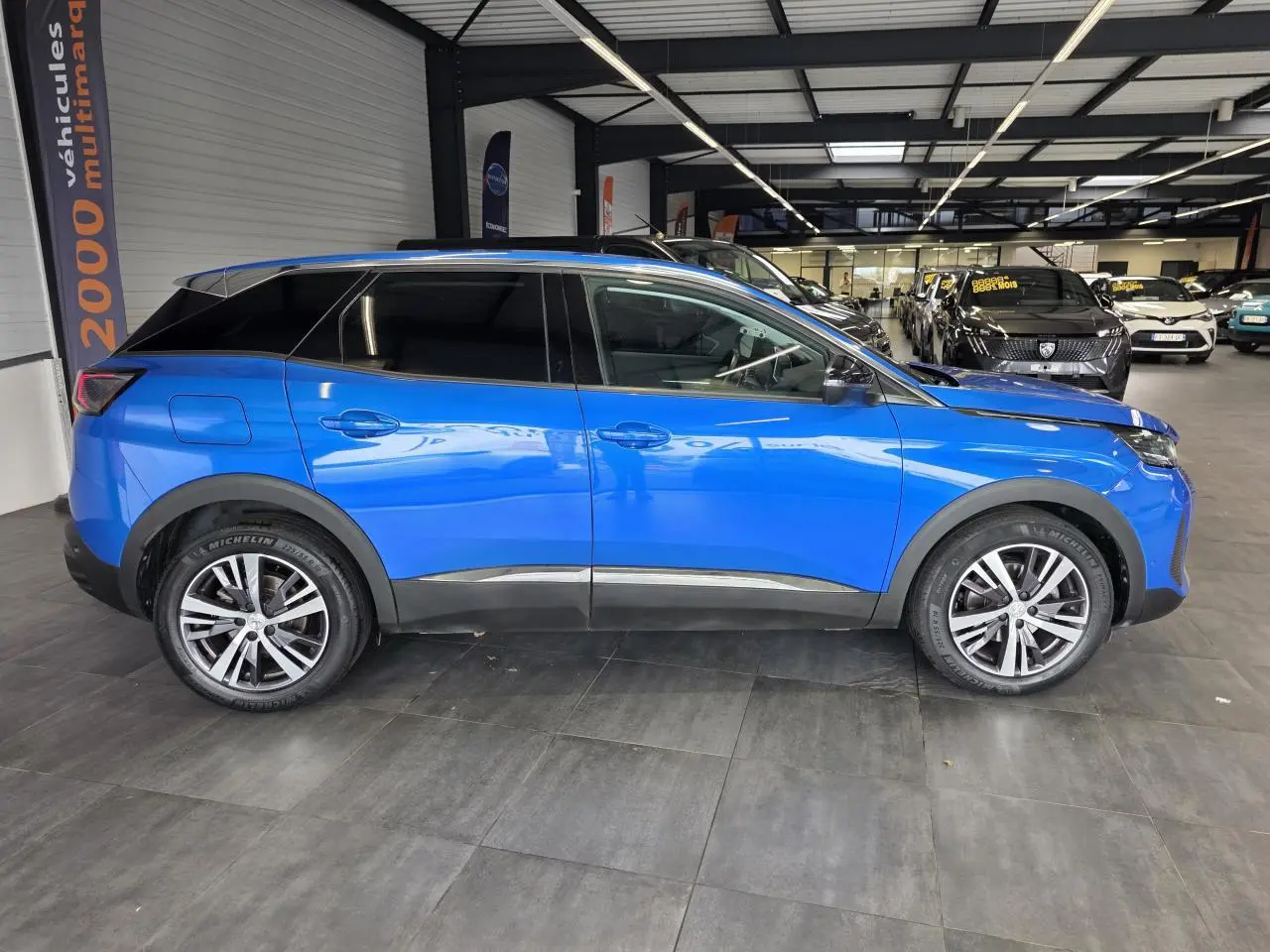 Vue de profil côté gauche d'un Peugeot 3008 2022 bleu Iron avec jantes alliage bicolores en showroom.